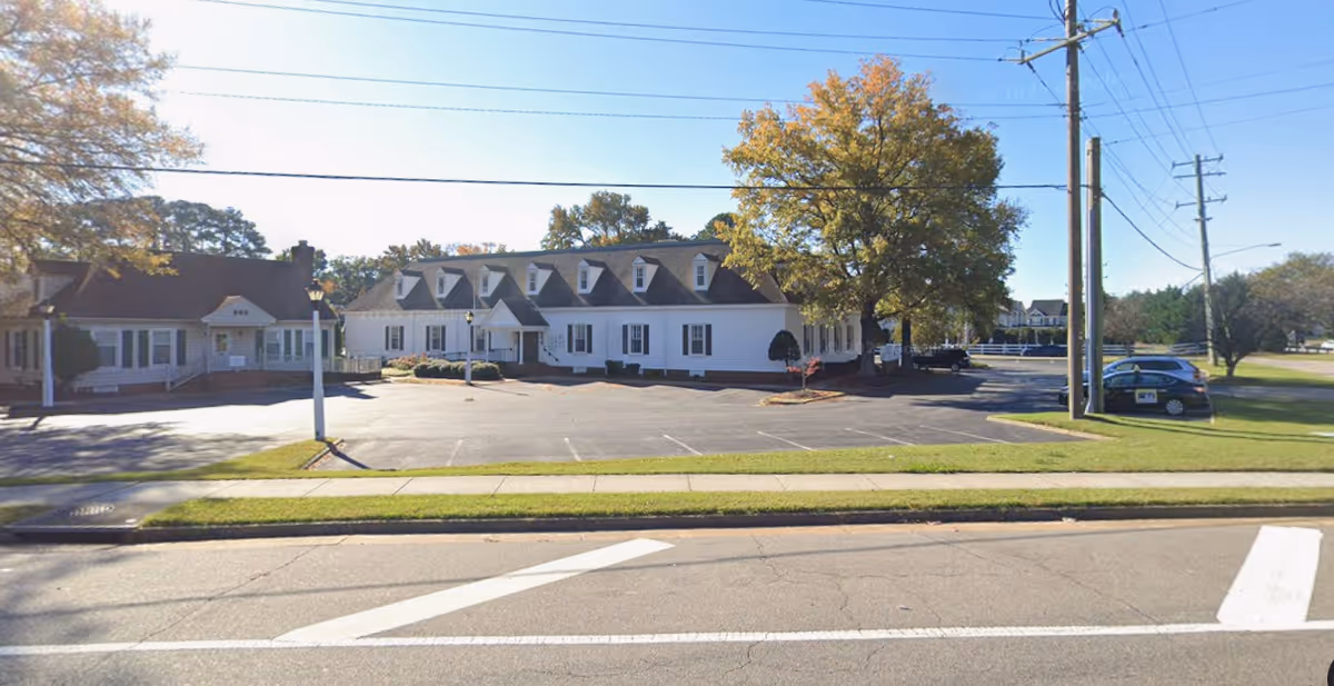 White, single-story senior living facility with a paved parking lot and trees.