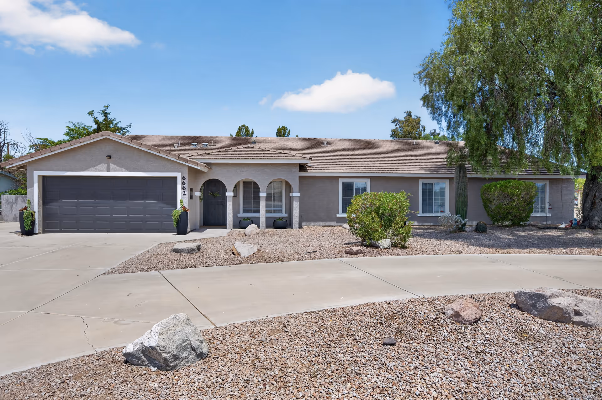 Single-story desert-style home with a two-car garage, arched entry, and gravel landscaping.
