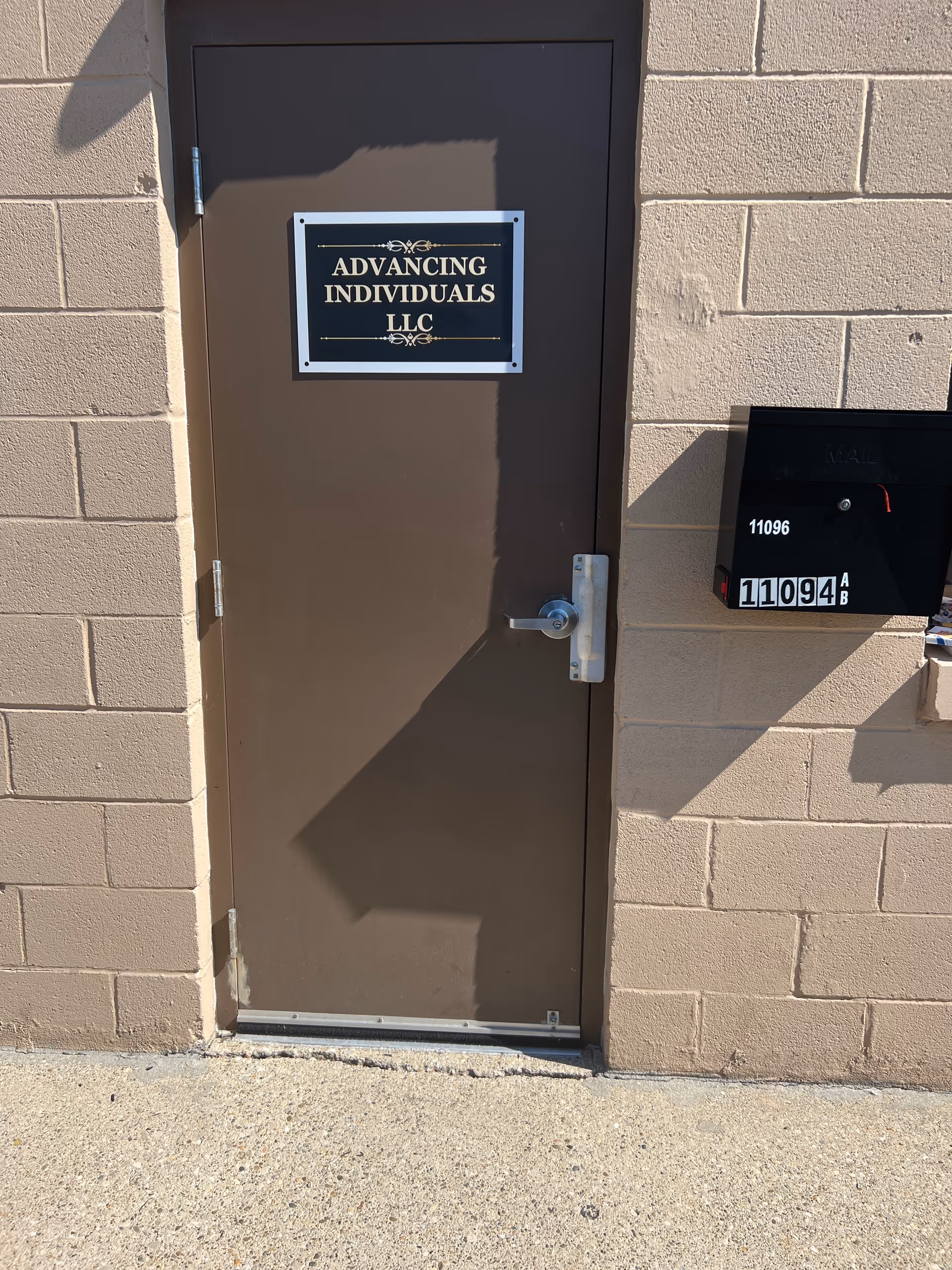 Exterior brown door with Advancing Individuals LLC sign, mailbox, beige brick wall visible.