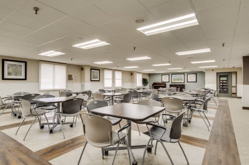 A spacious dining hall with many tables and chairs in a senior living facility.