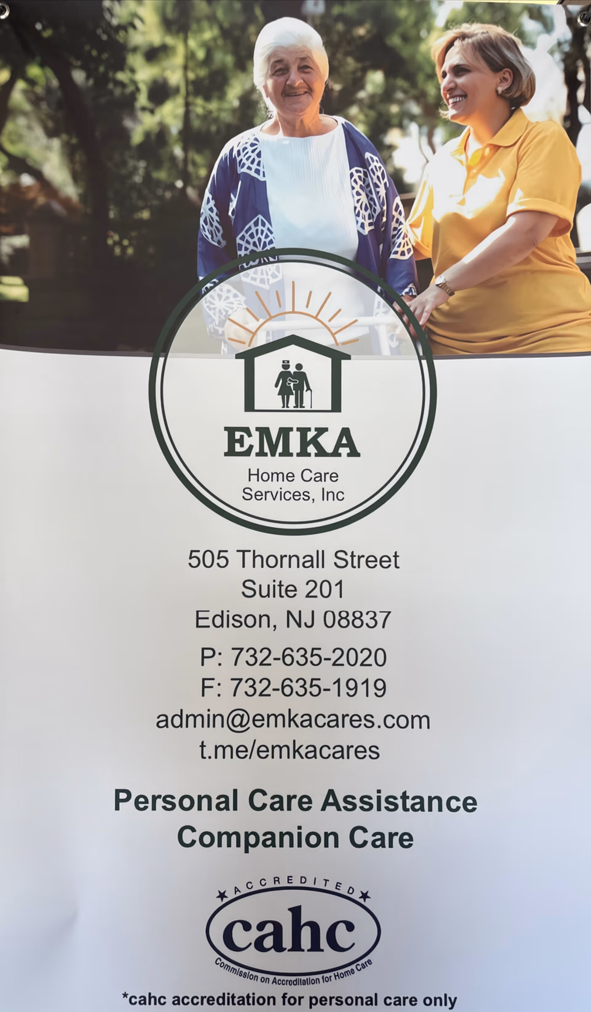 Two smiling people stand behind circular EMKA Home Care Services sign outdoors.