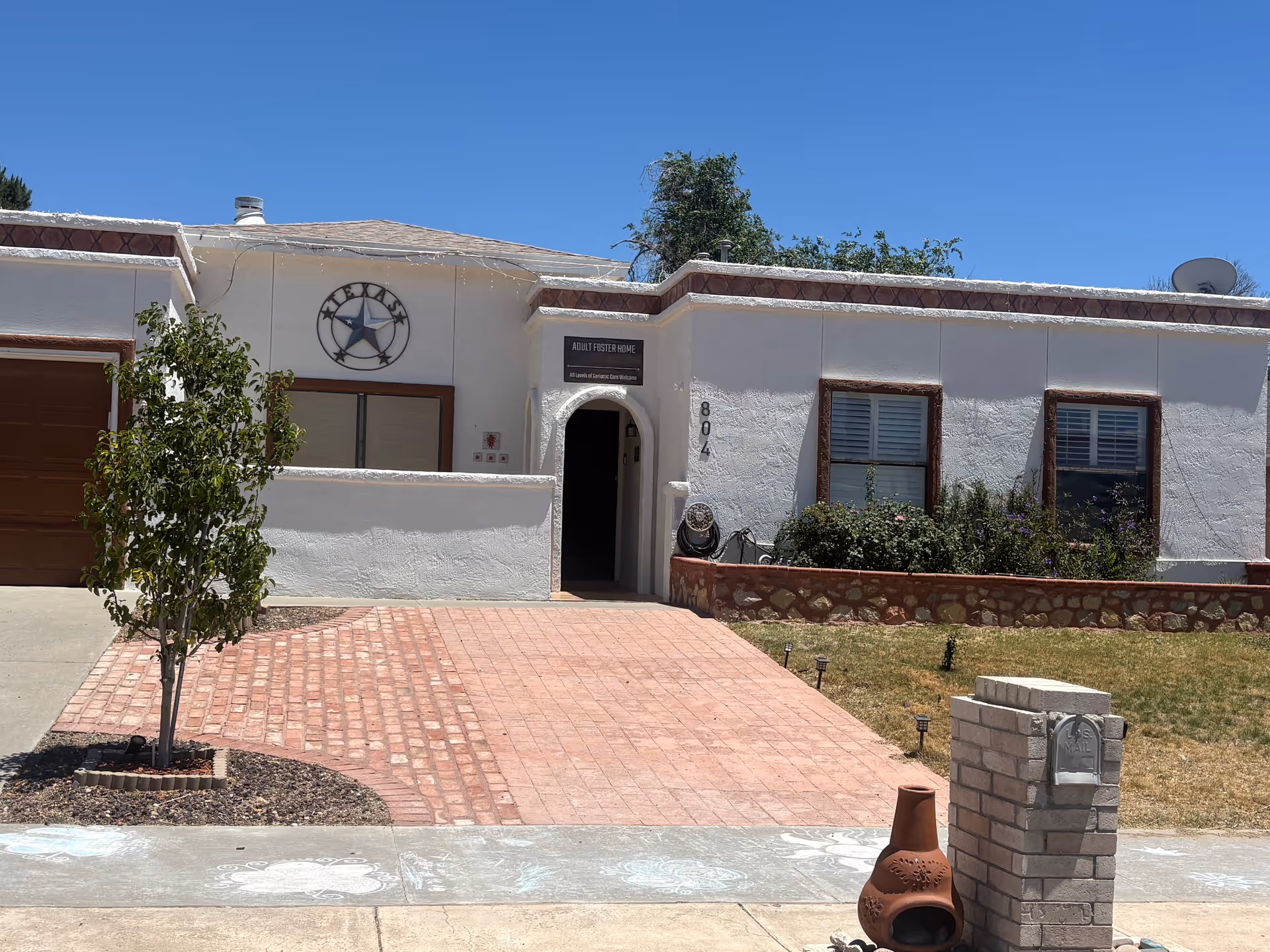 Exterior view of a single-story white building labeled Adult Foster Homes with a brick walkway.