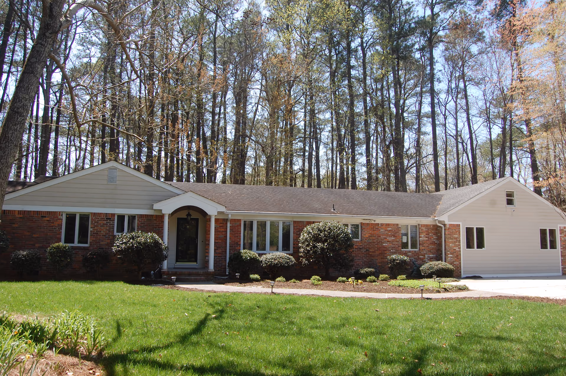 Single-story brick assisted living building with a manicured lawn and trees behind