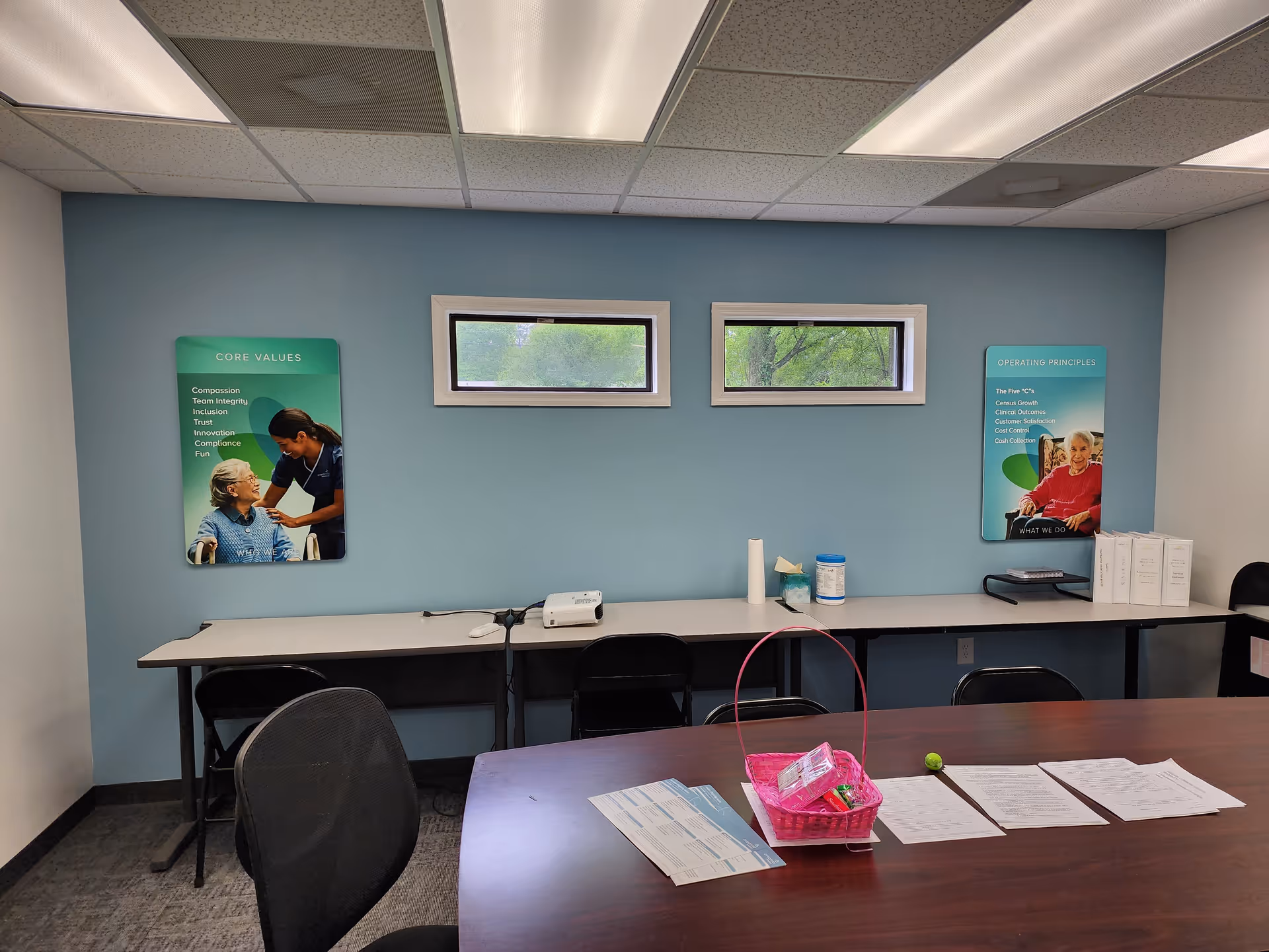 Interior meeting area with long table, chairs, paperwork, and wall-mounted posters.