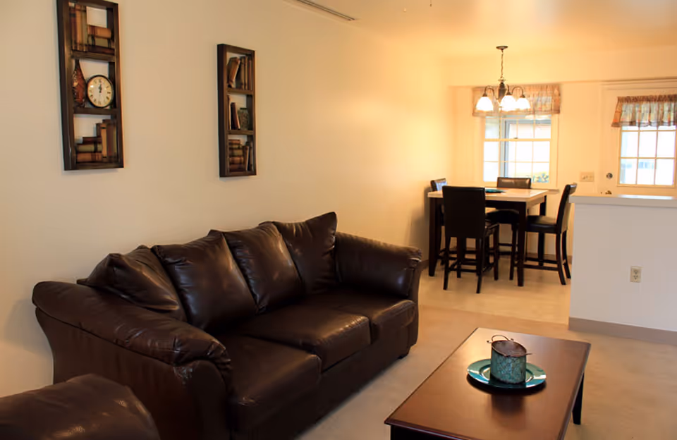 Open-plan living area with a brown leather sofa, coffee table, and a dining table visible in the background.