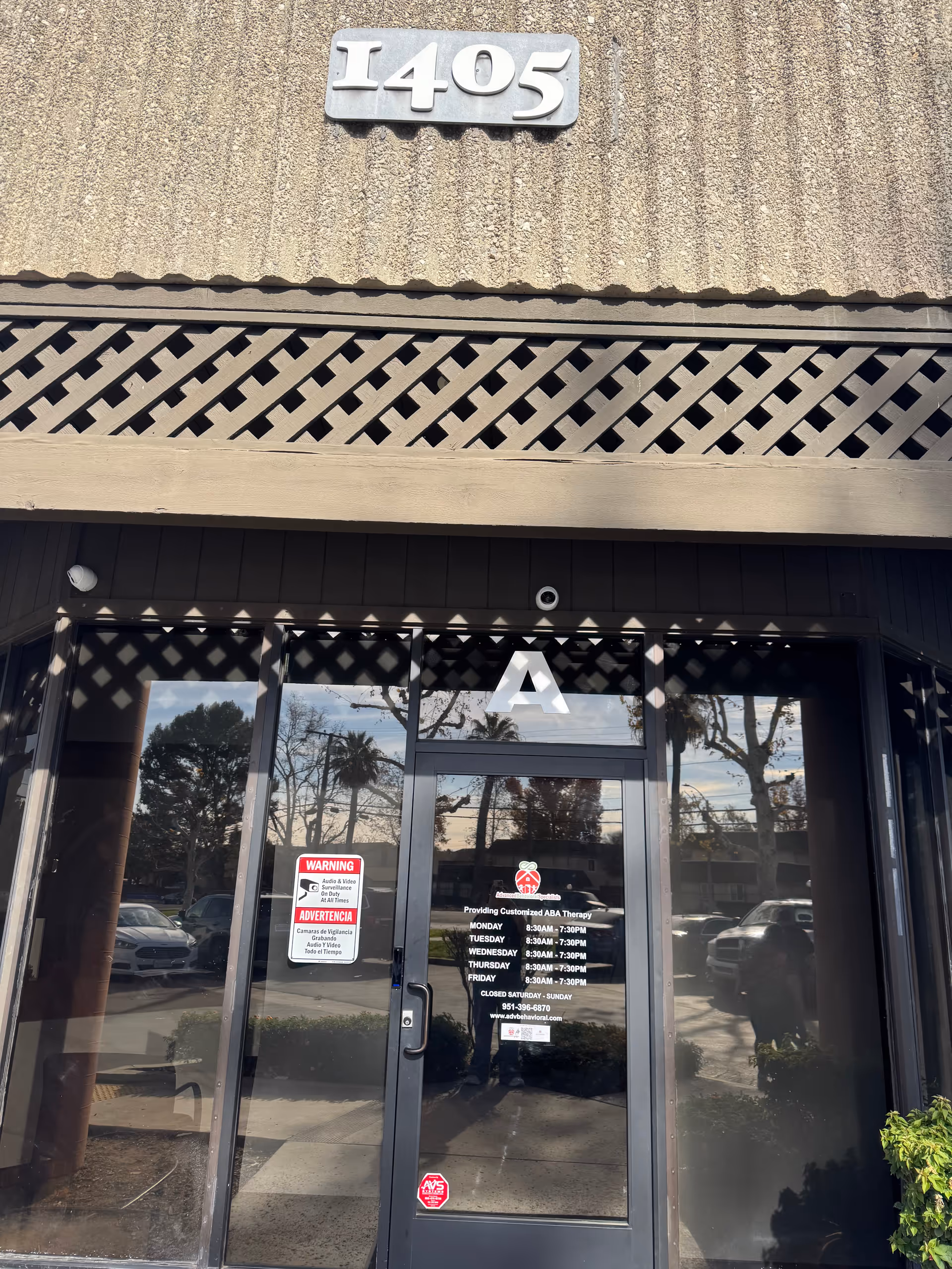 Front entrance of a building with glass doors and reflections of trees and cars.