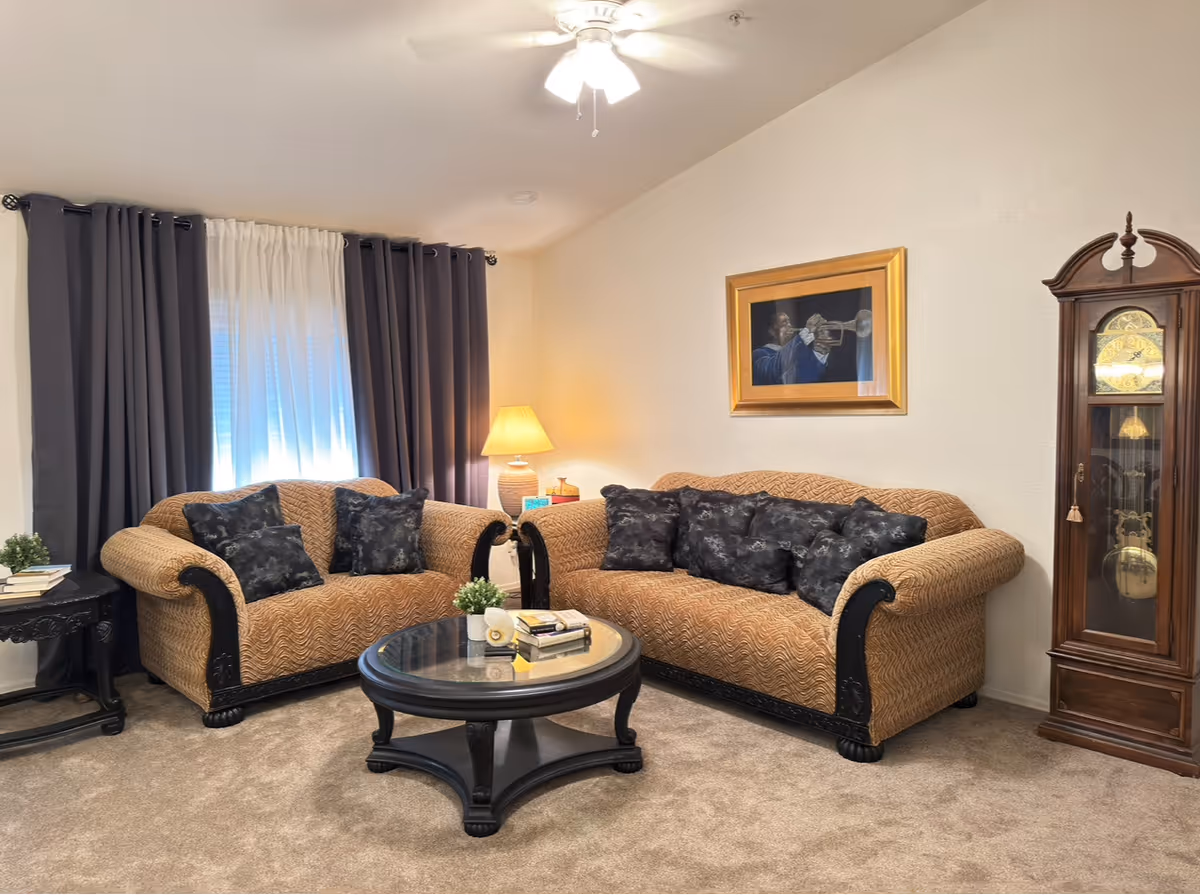 Two tan patterned sofas with dark cushions surround a glass coffee table in cozy living room.