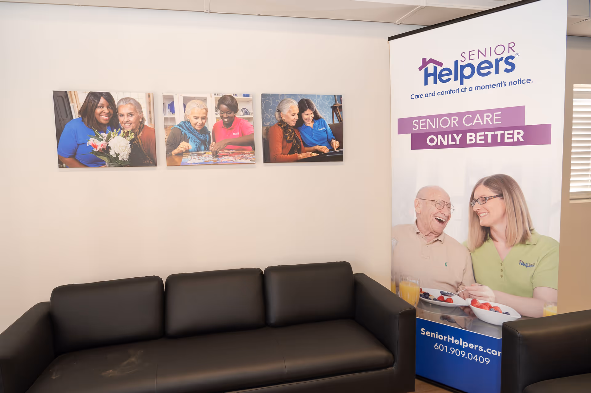 Interior lounge area with a black sofa, wall art, and a Senior Helpers banner.