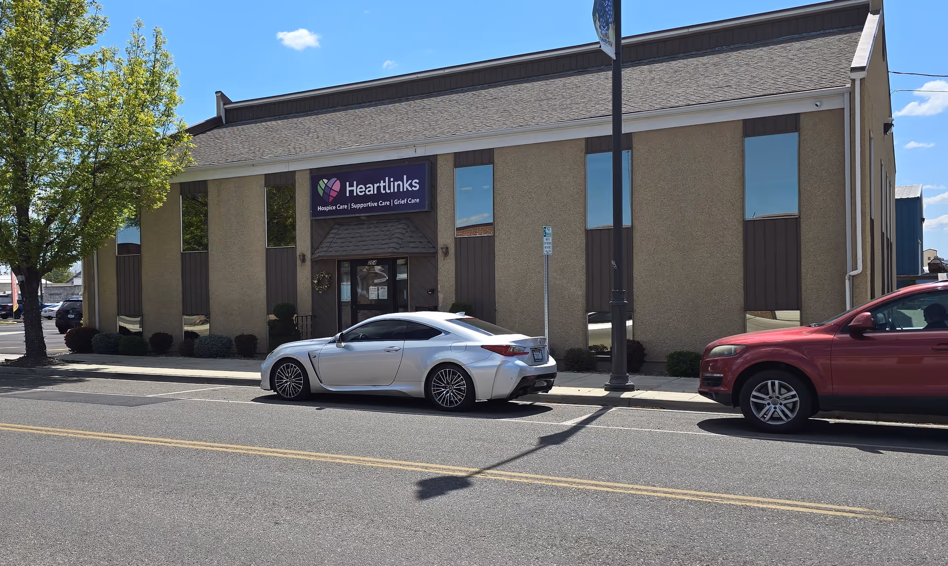 Exterior of Heartlinks facility with a sign, beige facade, and parked cars along the street.