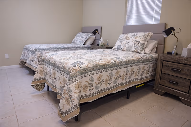 Two twin beds with matching quilted bedding in a neutral, tidy bedroom.