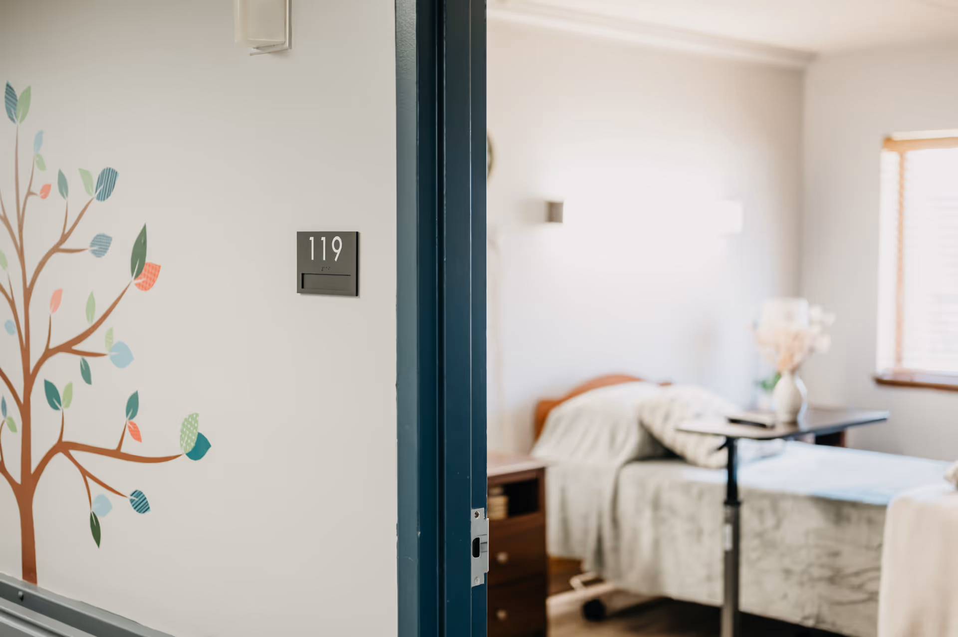 Open door reveals a resident bedroom with a bed, nightstand, and a wall mural.