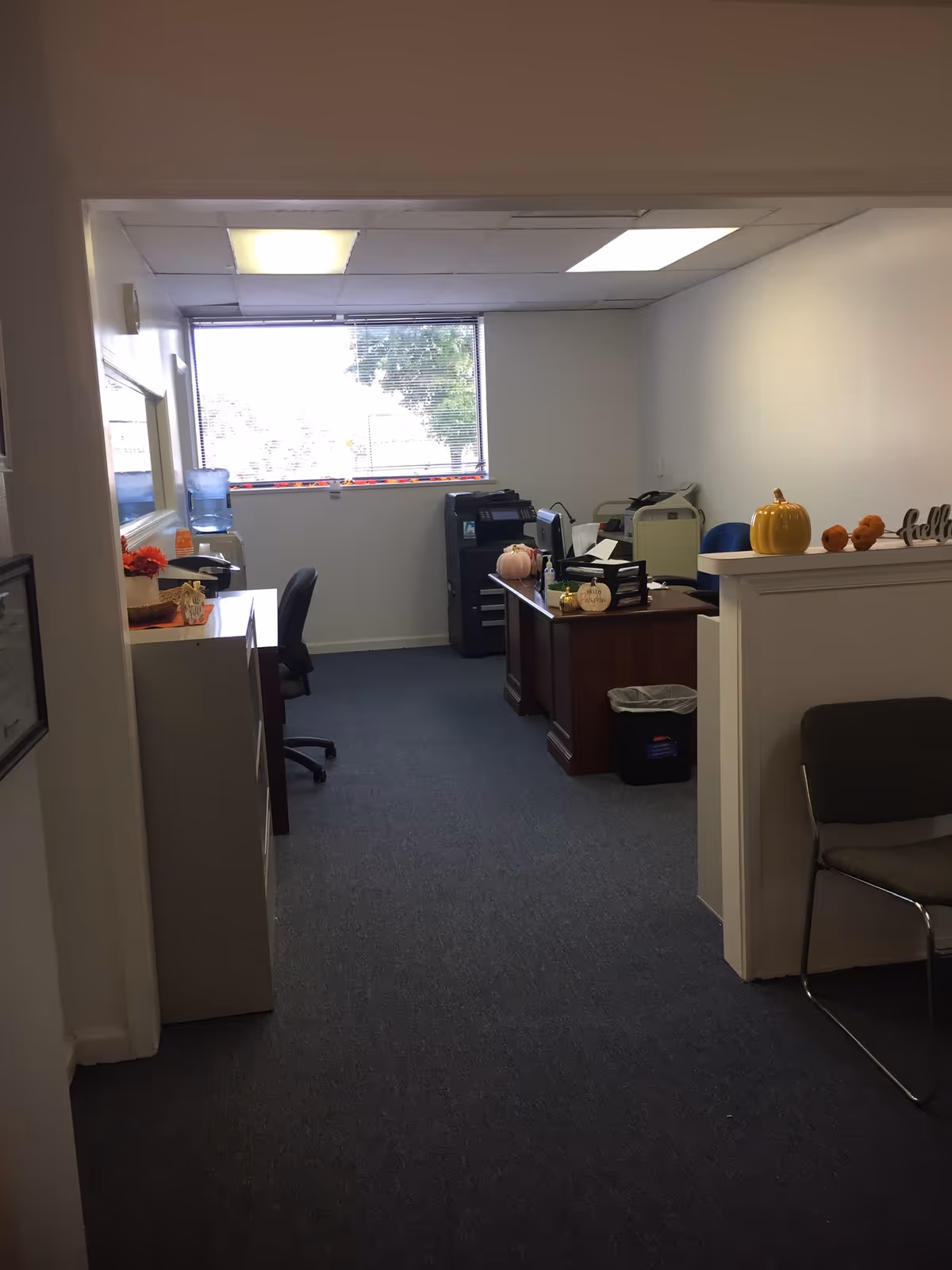 Interior office area with desks, printers, a window, and fall decorations.
