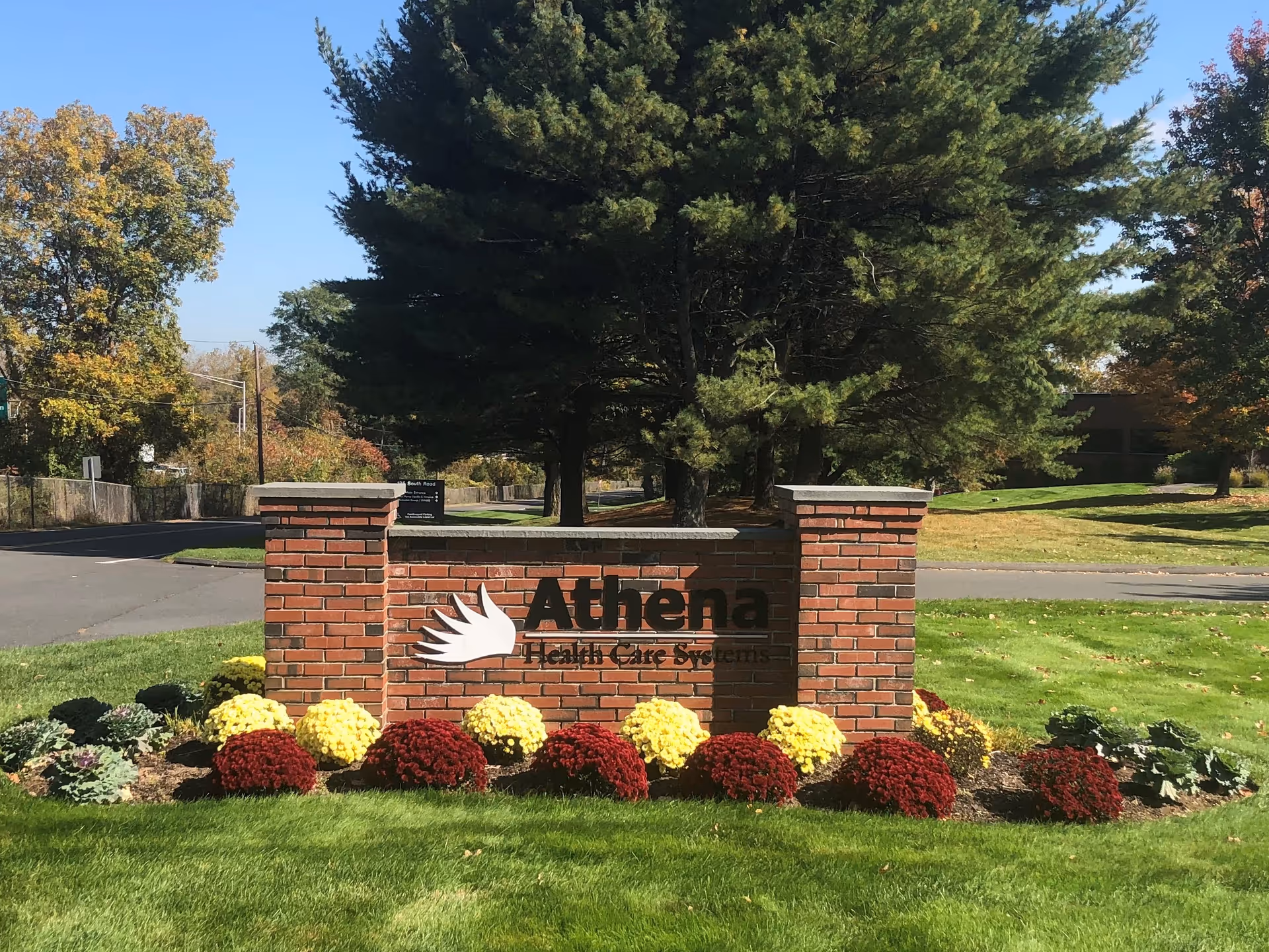 Brick entrance sign reads Athena Health Care Systems with landscaped flowers in front