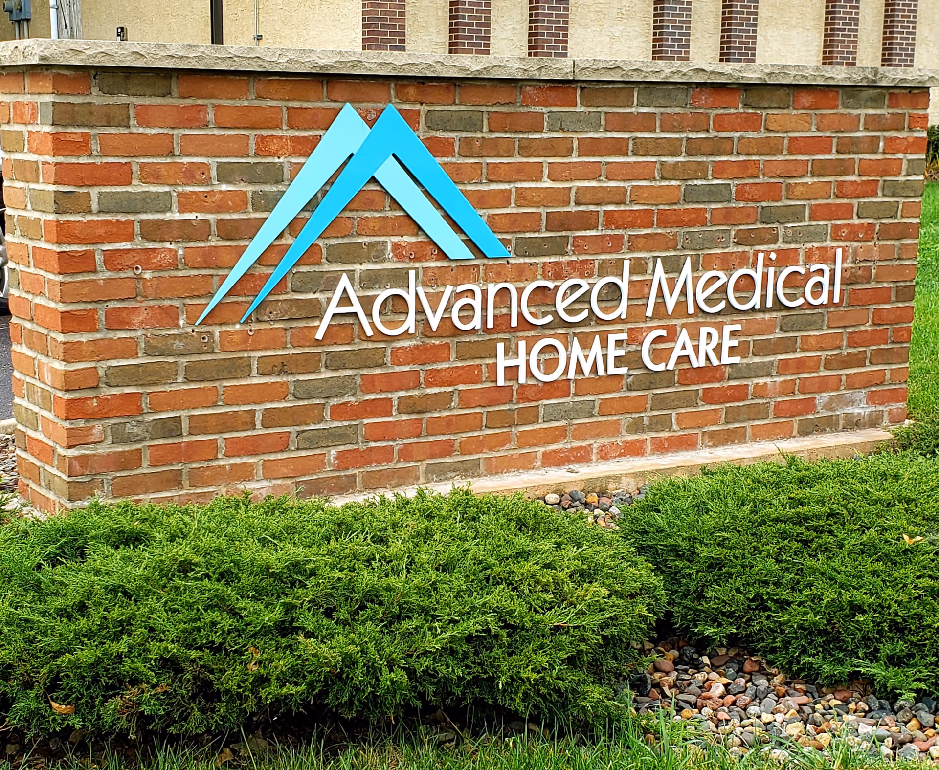 Brick sign for Advanced Medical Home Care with blue logo and landscaping.