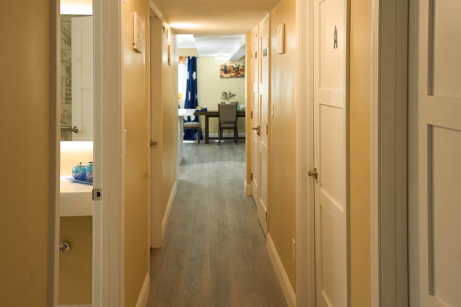 Interior hallway of a senior living facility leading to a dining area at the end.