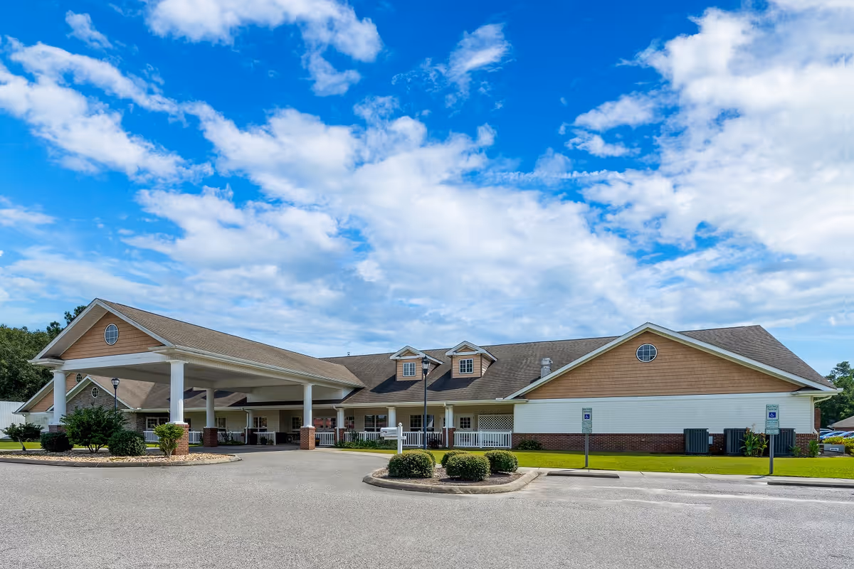 Single-story senior living facility with a covered entrance and neatly landscaped front under a blue sky.