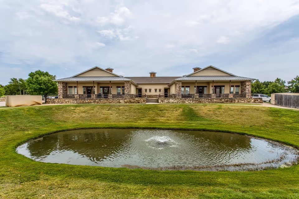 A single-story retirement facility with stone accents and a circular pond in front.