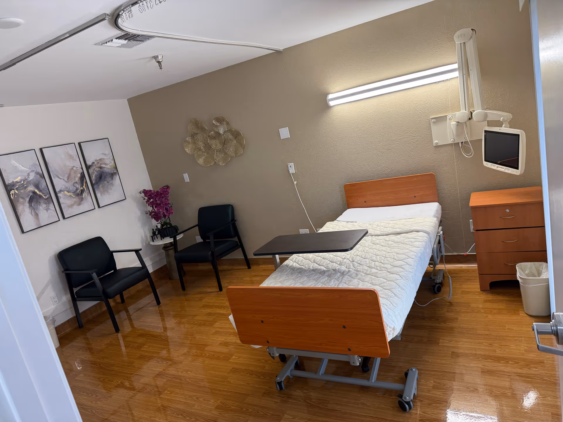 Hospital-style patient bed in a small room with monitor, dresser, and seating.