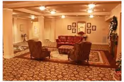 A cozy living room lounge with patterned carpet, several chairs, a red sofa, and wall art.