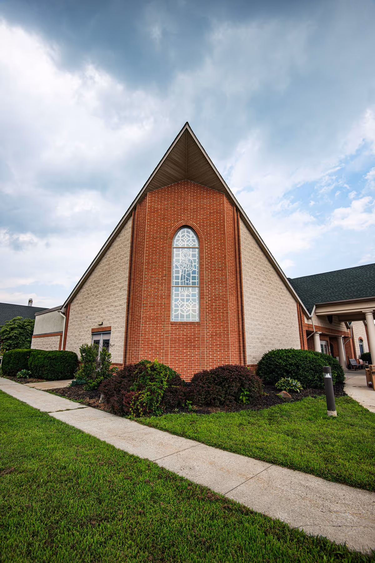 Brick nursing facility exterior with tall arched window and landscaped lawn.
