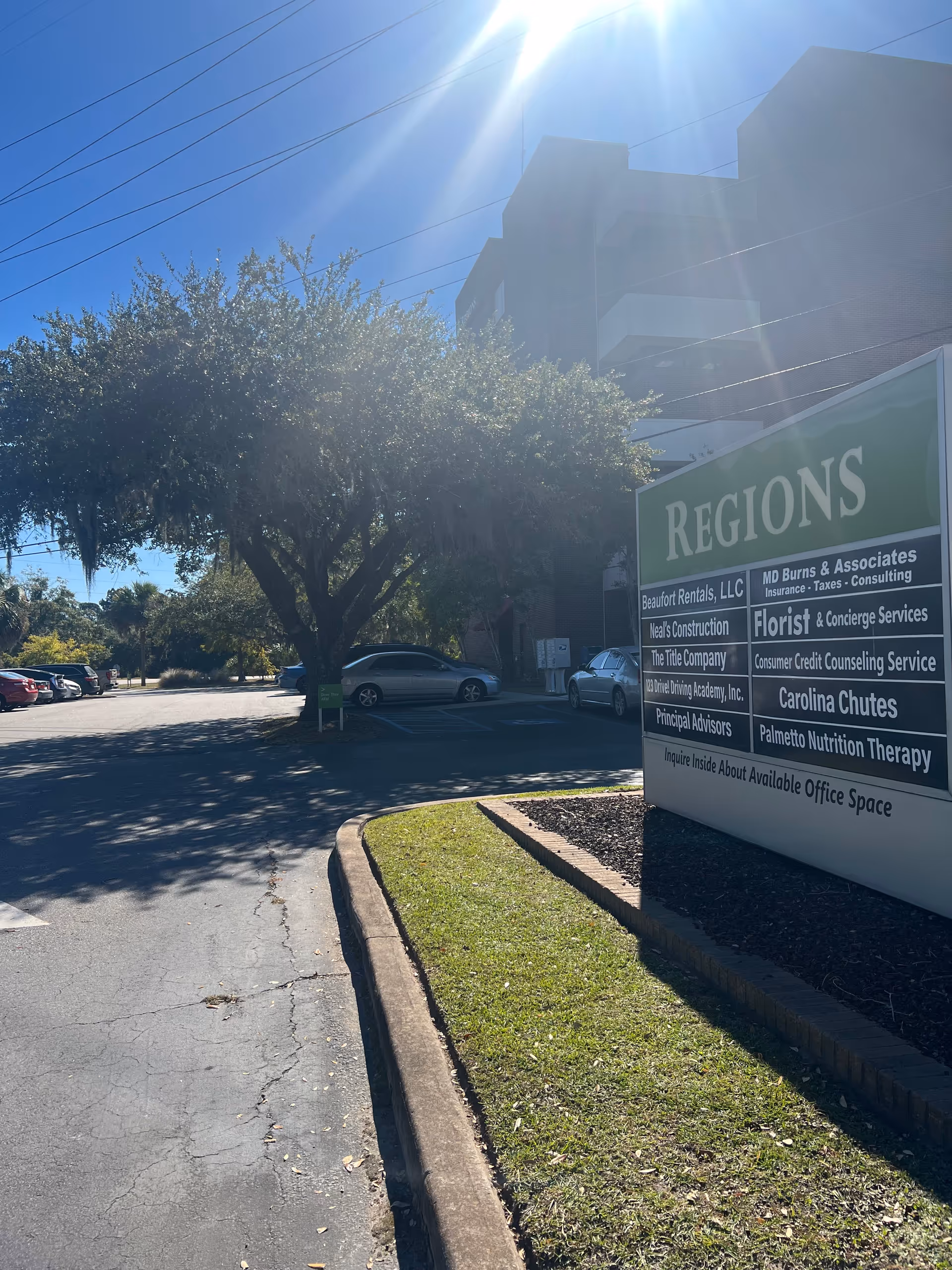 Sunny parking lot with a large Regions sign and a tree in front of a building.