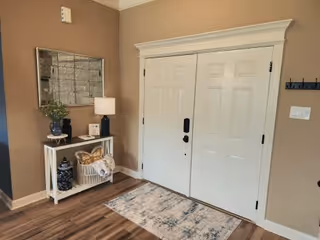 Entry foyer with double white doors, a console table, lamp, mirror, and rug.