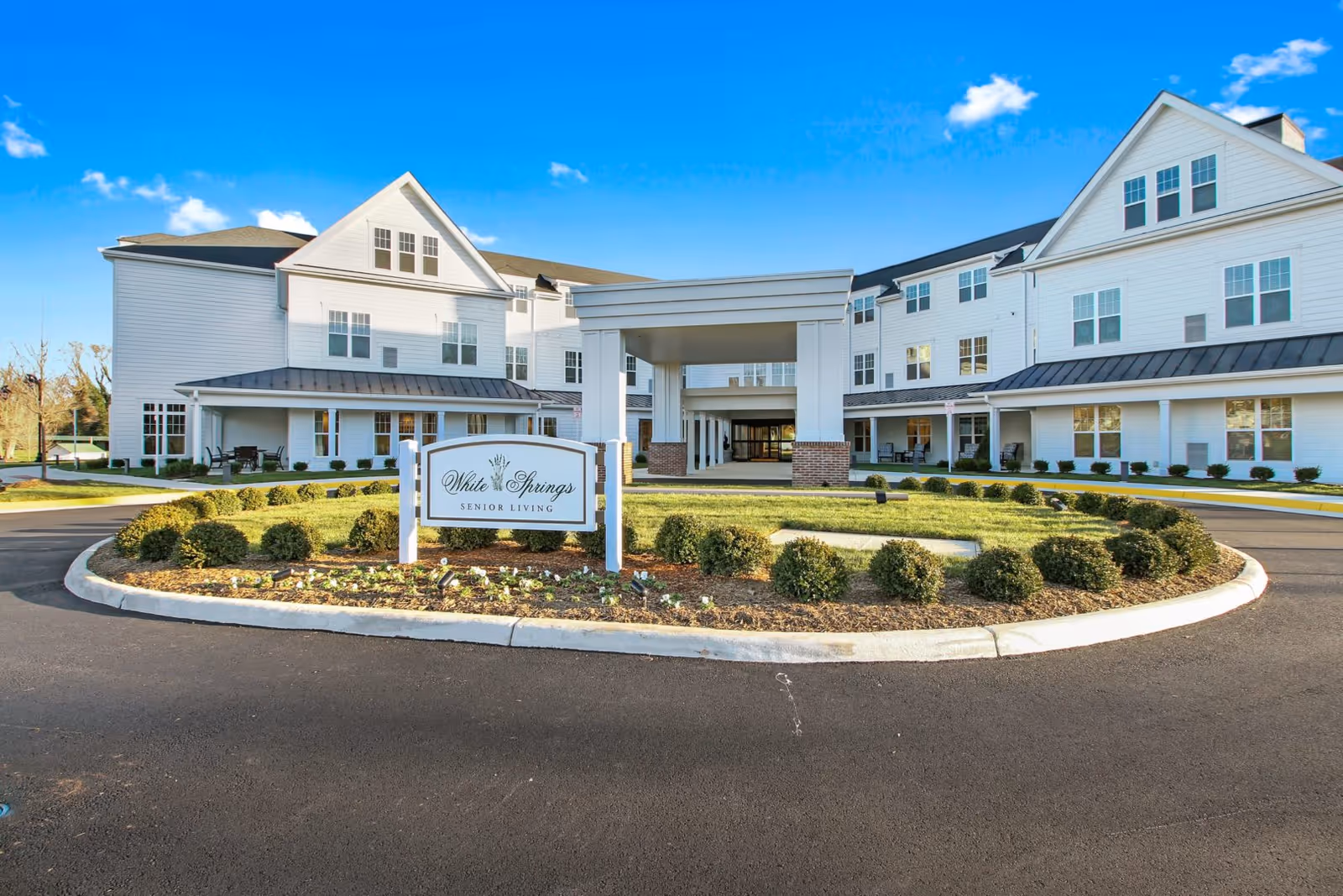 Front entrance of the White Springs Senior Living building with a circular driveway and landscaped sign in the center.