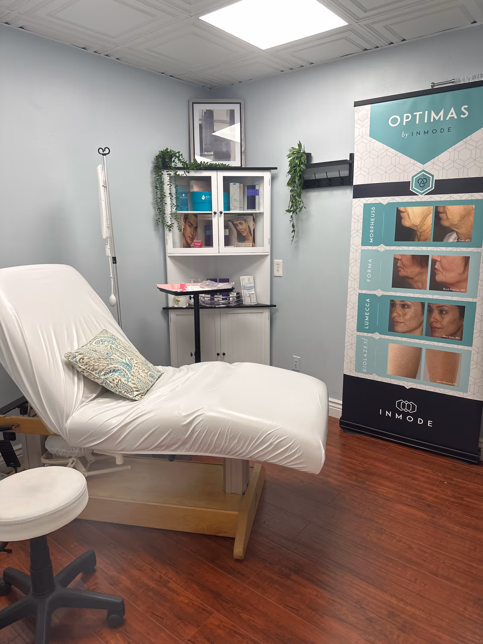 A clean medical treatment room with an adjustable bed, IV stand, cabinet, and promotional banner.