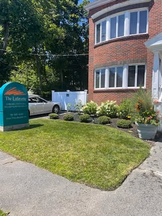Brick building with arched window, front lawn, sign reading The Lafayette Rehabilitation beside shrubs.