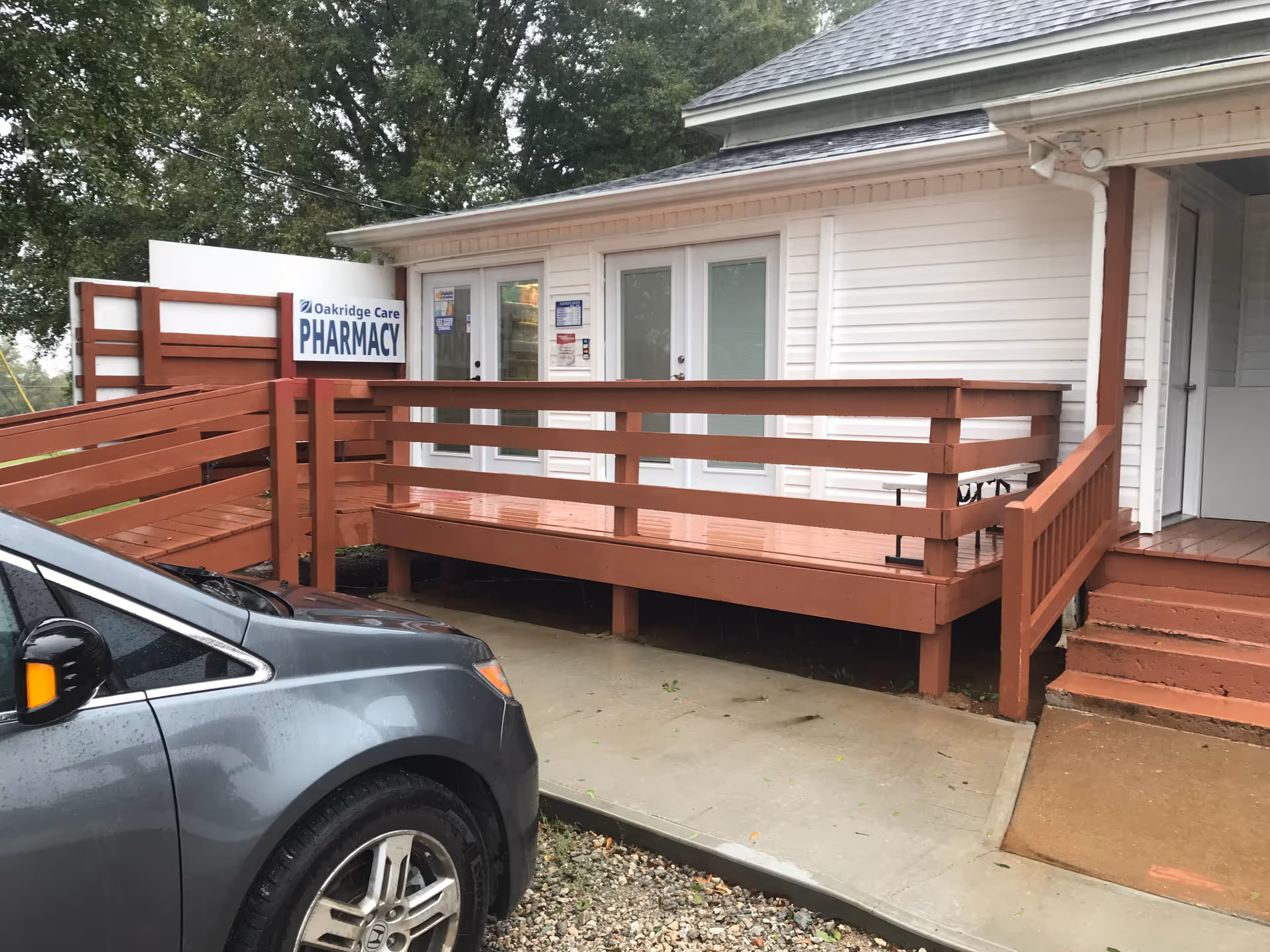 White single-story building with a red wooden ramp and Oakridge Care Pharmacy sign