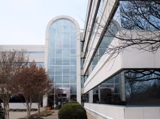 Modern glass-front building with curved archway entrance and surrounding trees.