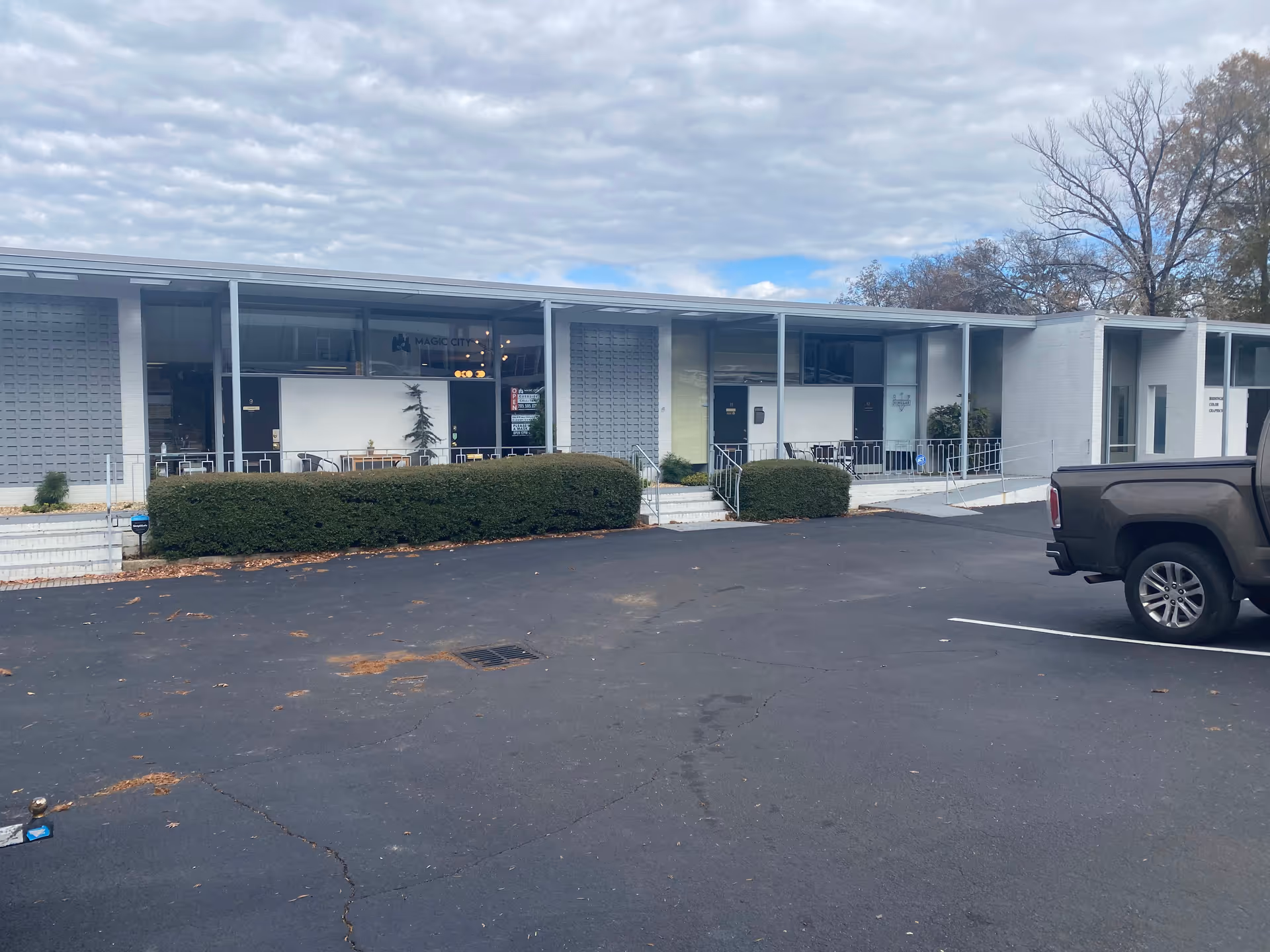 Long, low, modern building with glass storefronts, hedges, and a paved parking lot.