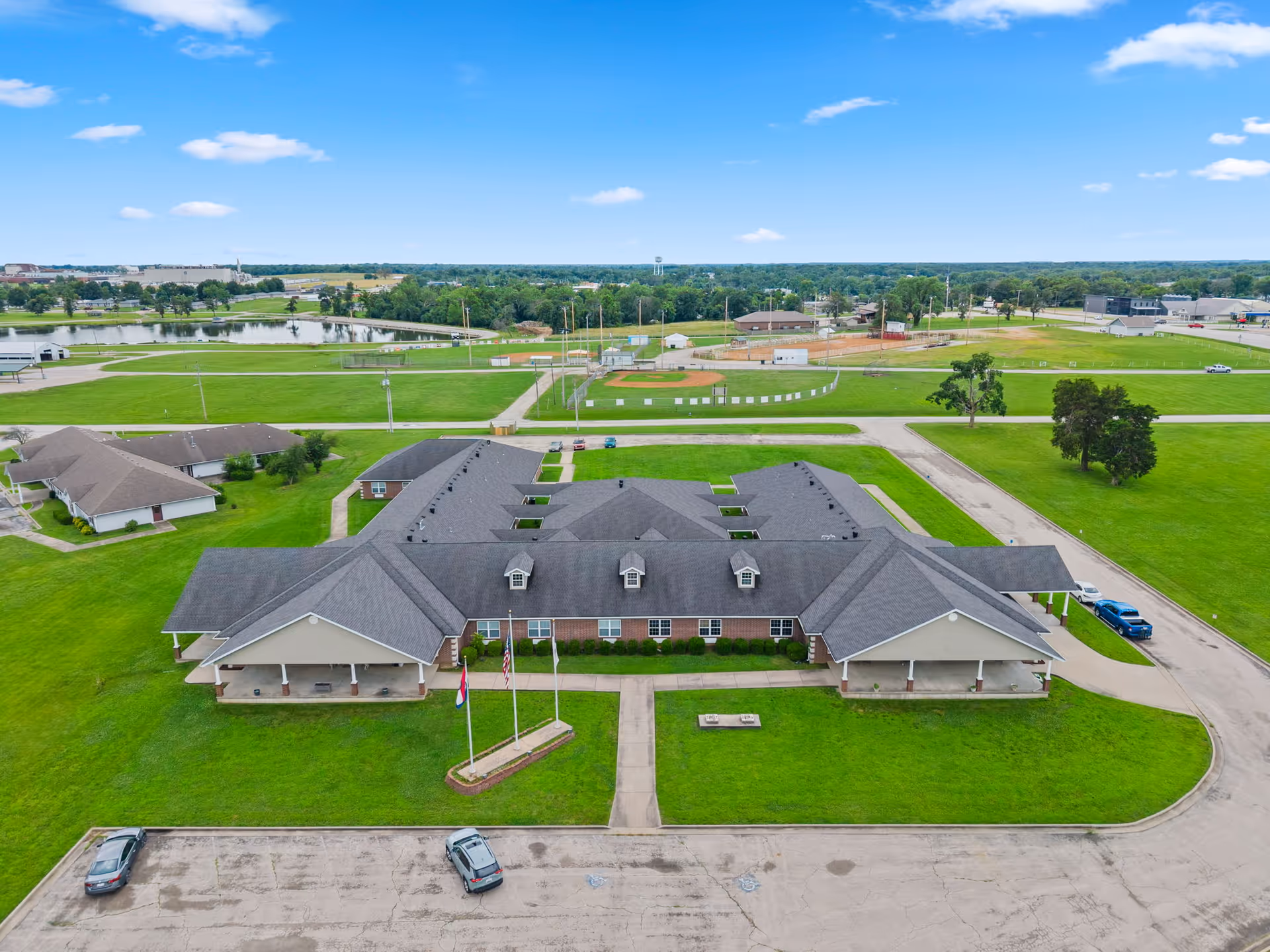 Aerial view of a large L-shaped senior living facility with green lawns and parking.