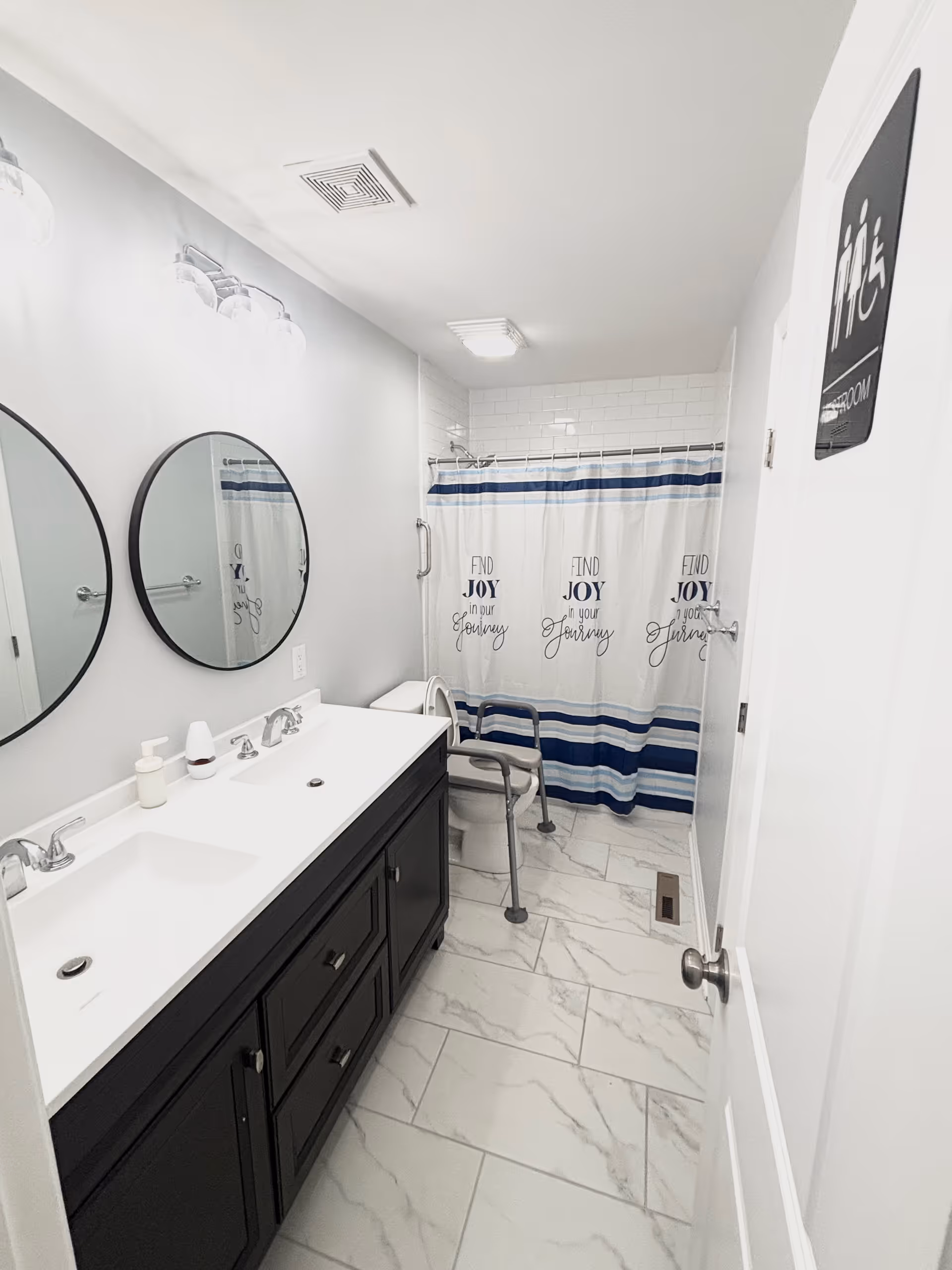 Modern shared bathroom with double vanity, round mirrors, and blue striped shower curtain.