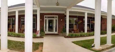 Brick senior living facility entrance with white columns and a walkway.