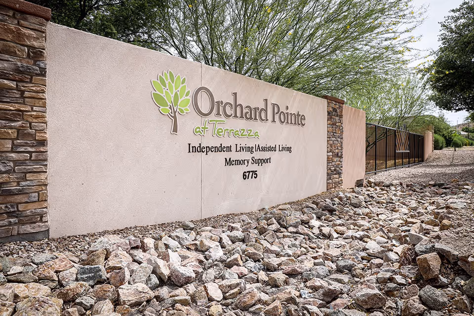 Exterior sign for Orchard Pointe at Terrazza with stone wall and rocky landscaping.