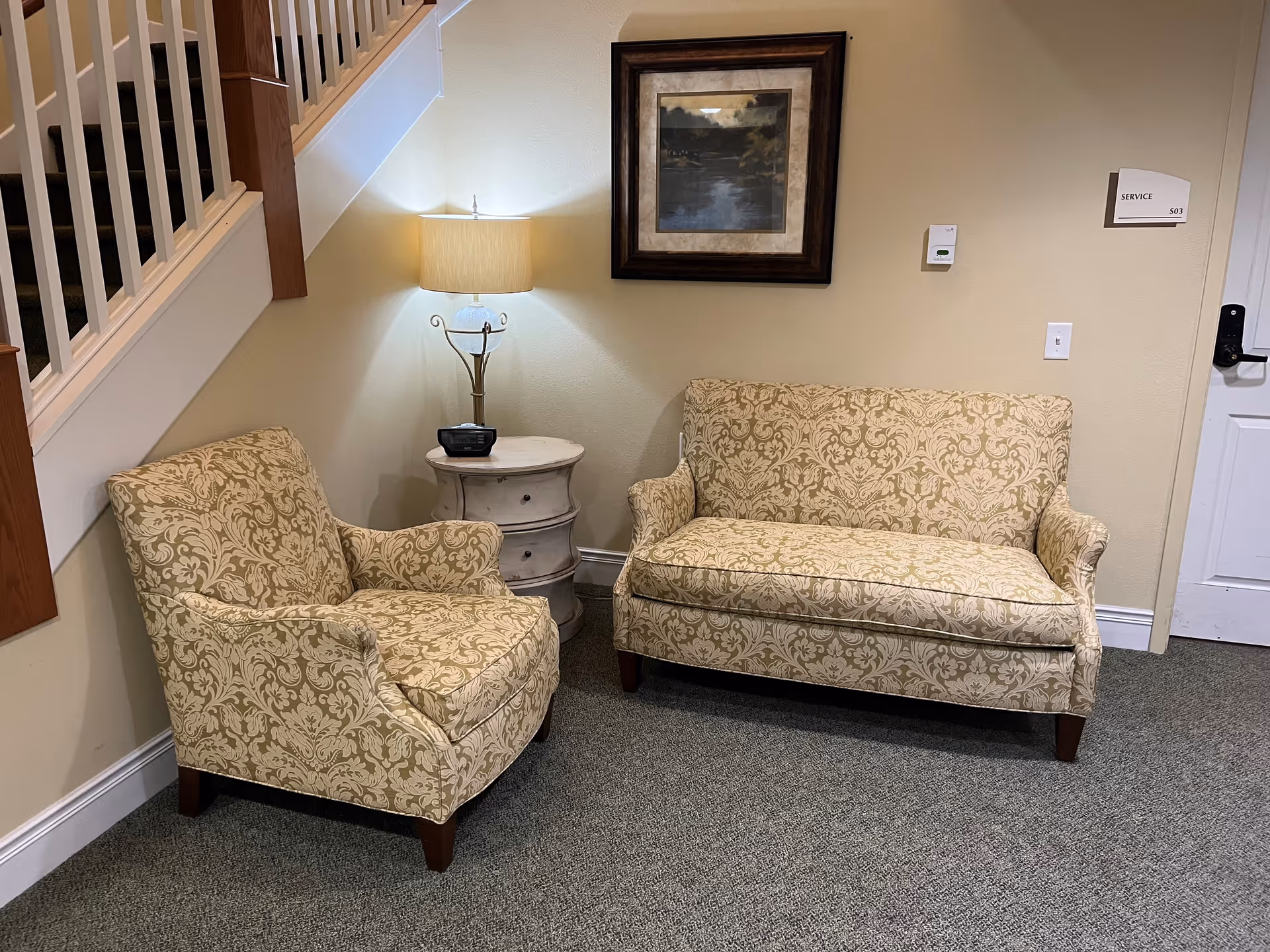 Cream patterned loveseat and armchair with lamp and framed art in a cozy lobby seating area.