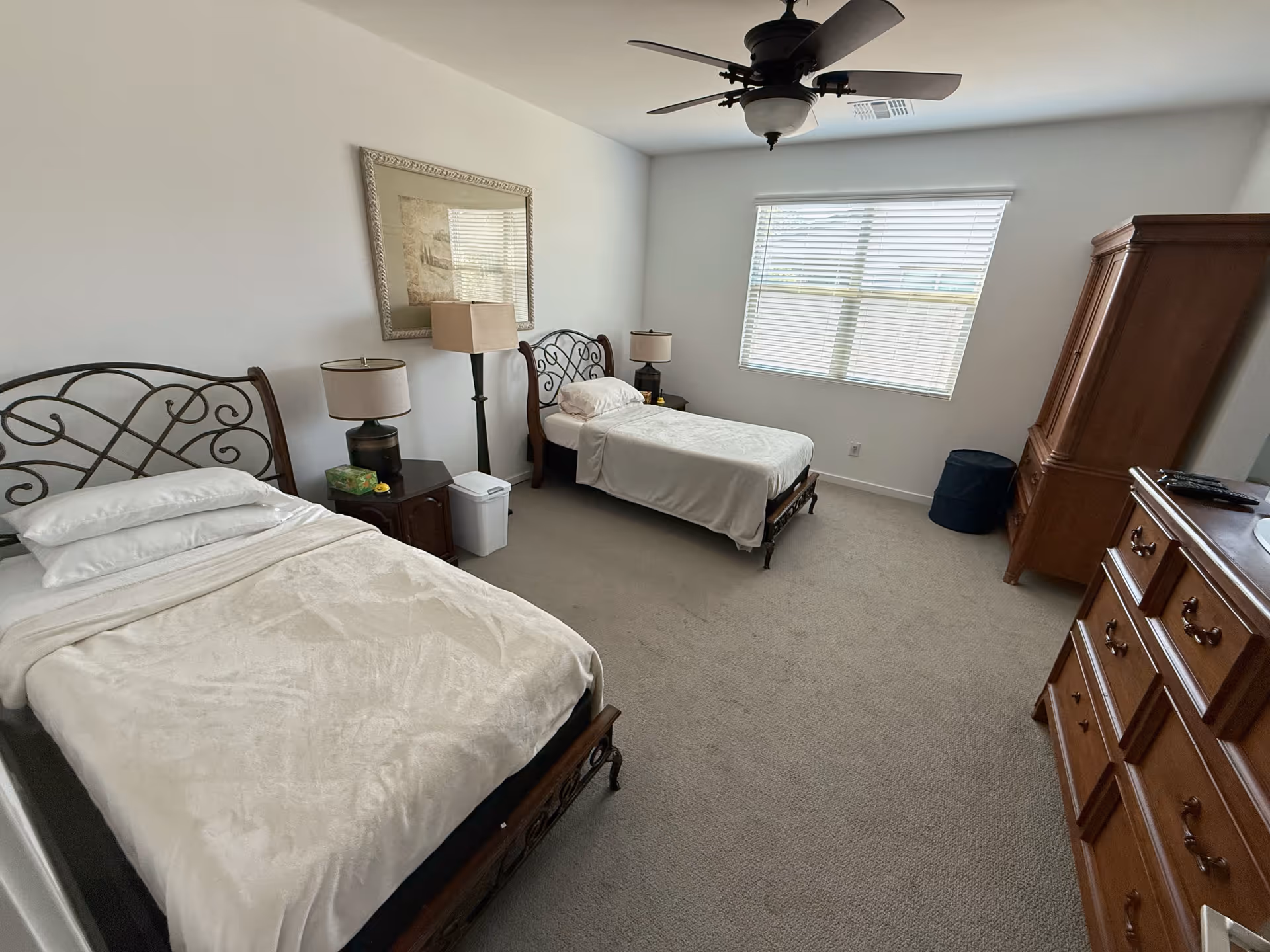 Two single beds with metal headboards, nightstands, and a wooden armoire in a bedroom.
