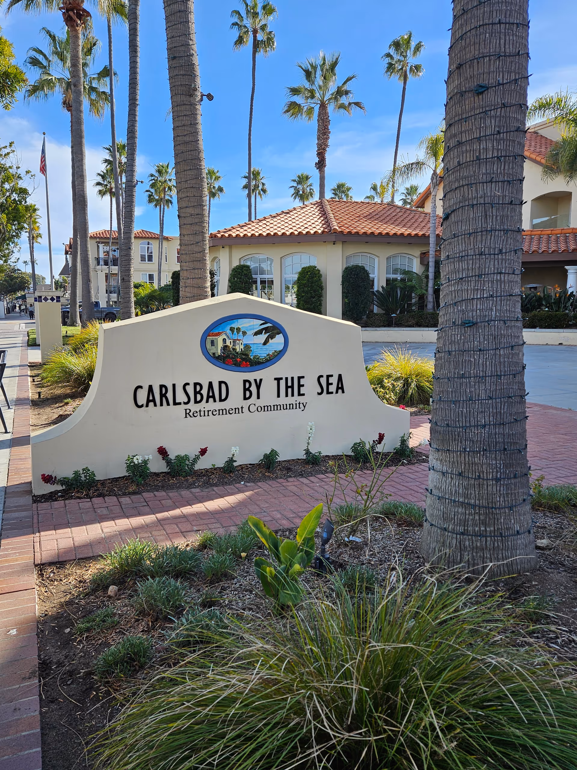 Exterior view of Carlsbad by the Sea retirement community sign with palm trees