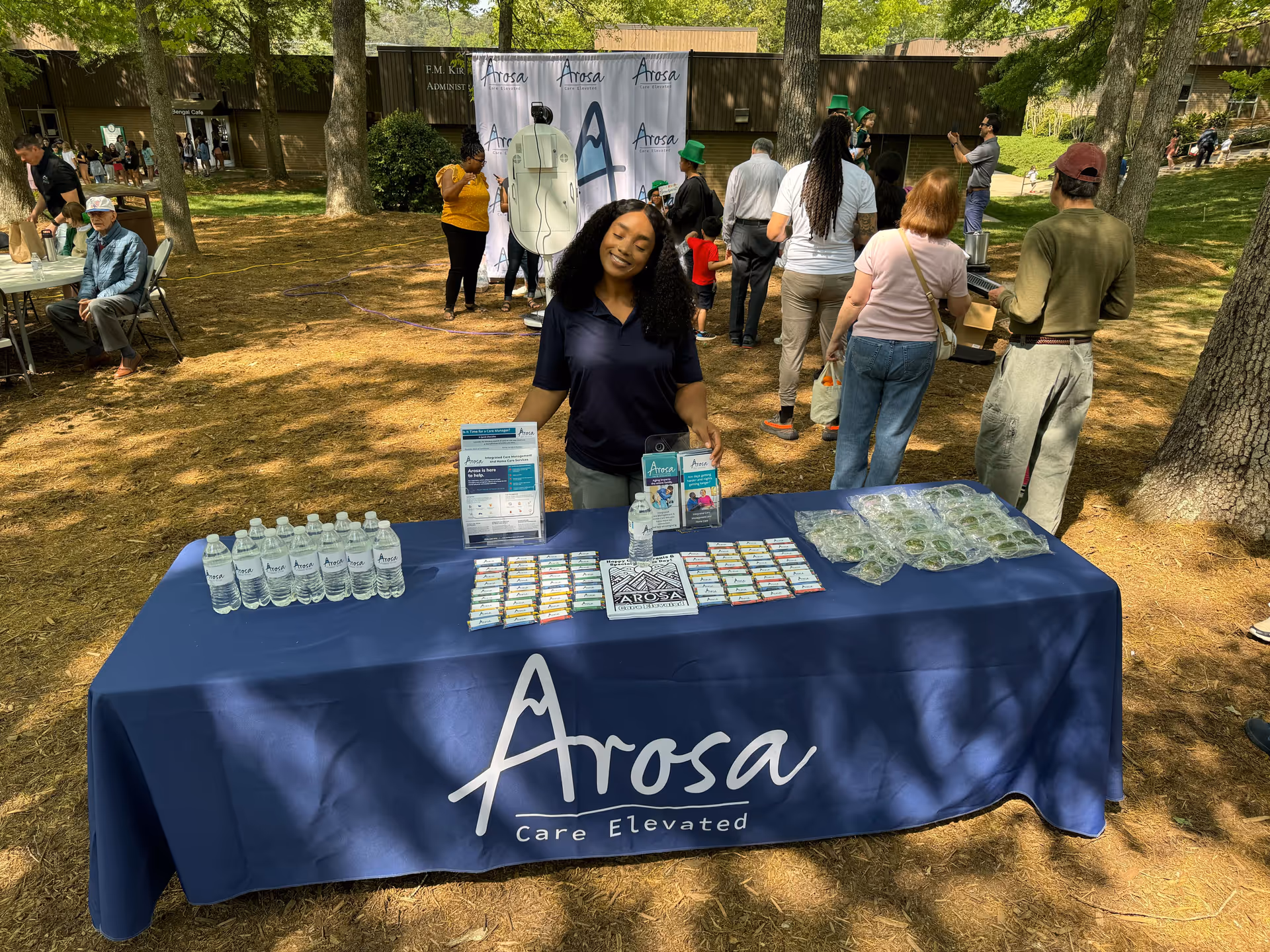 Outdoor event with a staffed Arosa Piedmont Triad information table and attendees.