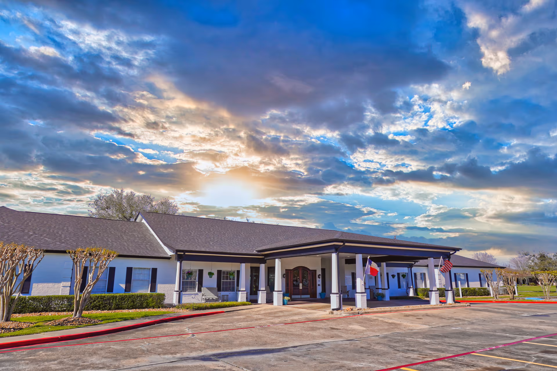 Single-story senior living facility with a covered entrance and flags under a cloudy sky.
