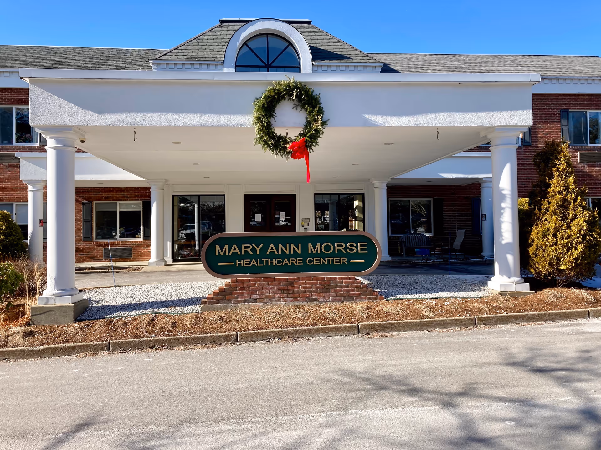 Front entrance of Mary Ann Morse Healthcare Center showing a covered portico with columns, a wreath, and the facility sign.