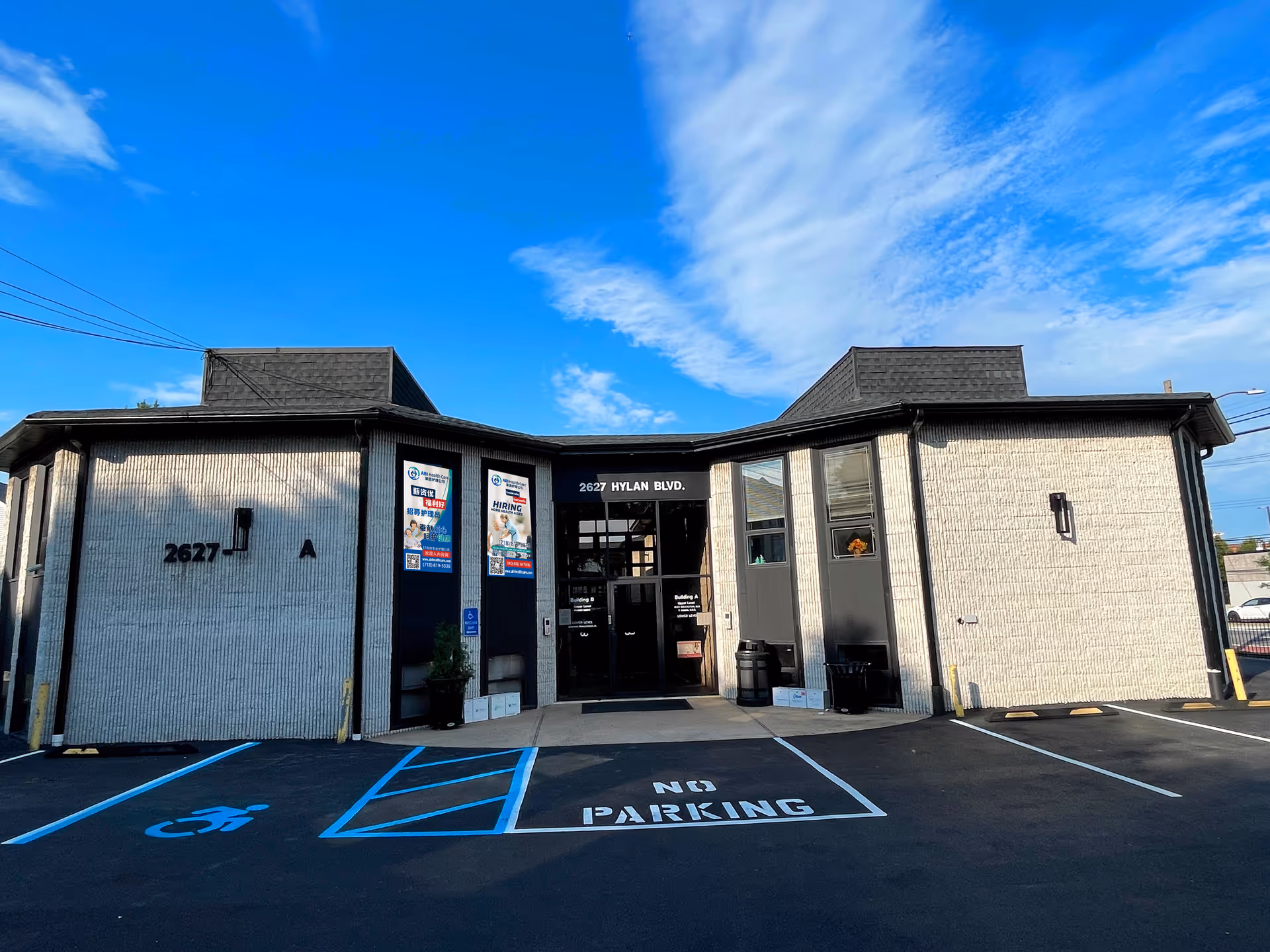 Exterior view of a single-story building with glass entrance and parking lot under a blue sky