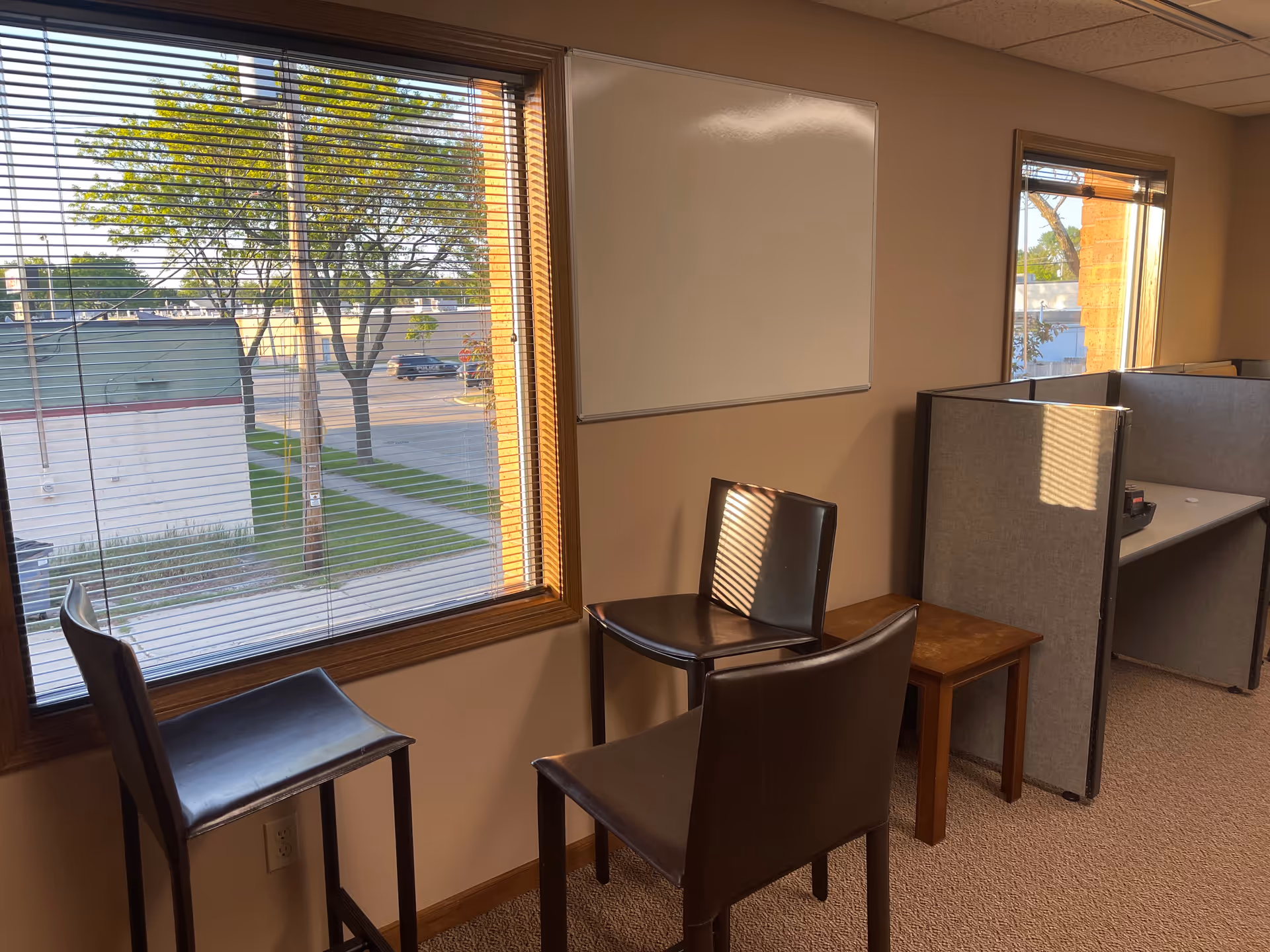 Interior office area with chairs, a whiteboard, and cubicle desks by a window.