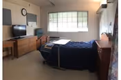 A small furnished bedroom with a hospital-style bed, dresser, TV, and a window.