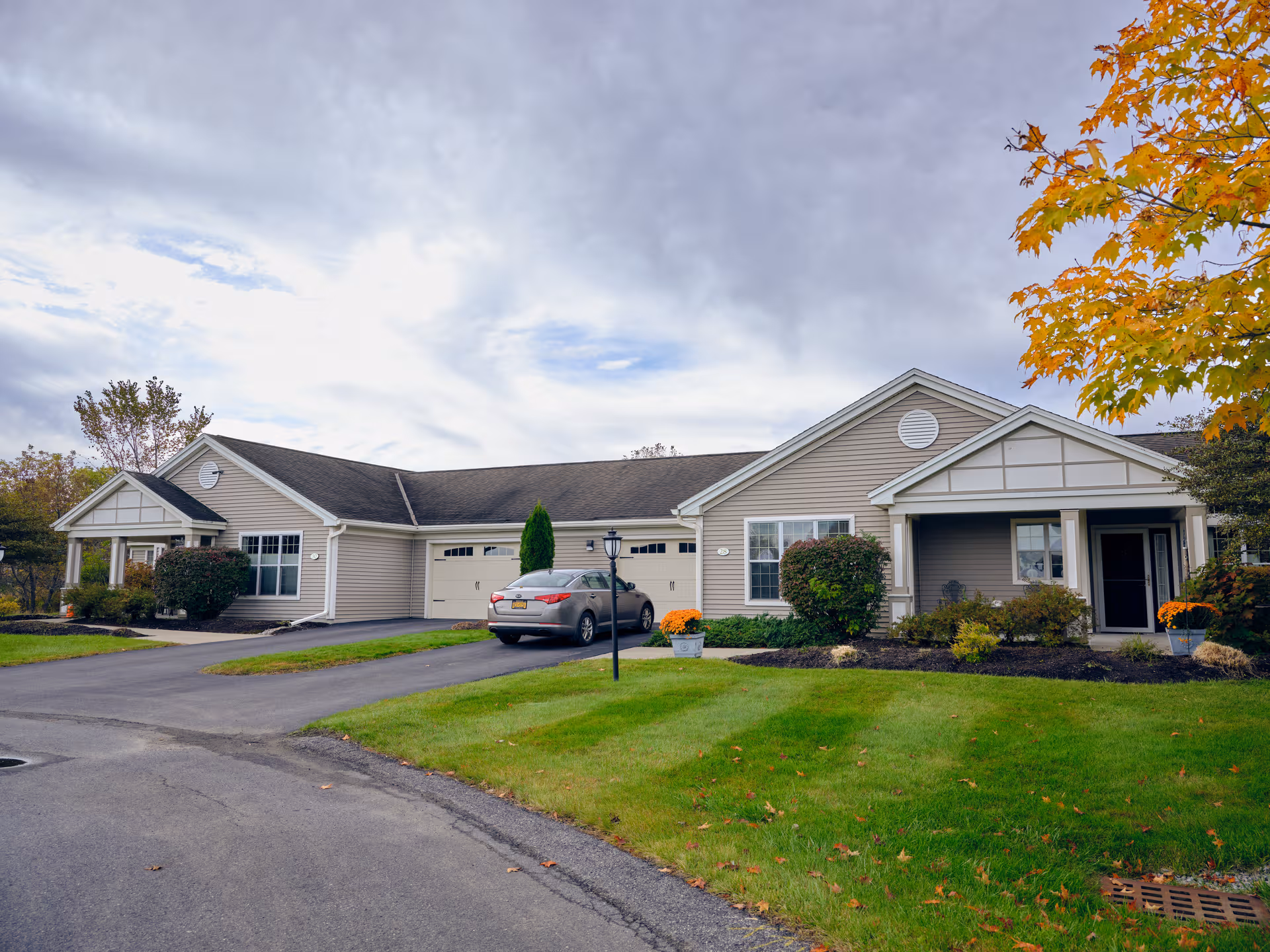 Front view of a single-story senior living facility with garages and a car.