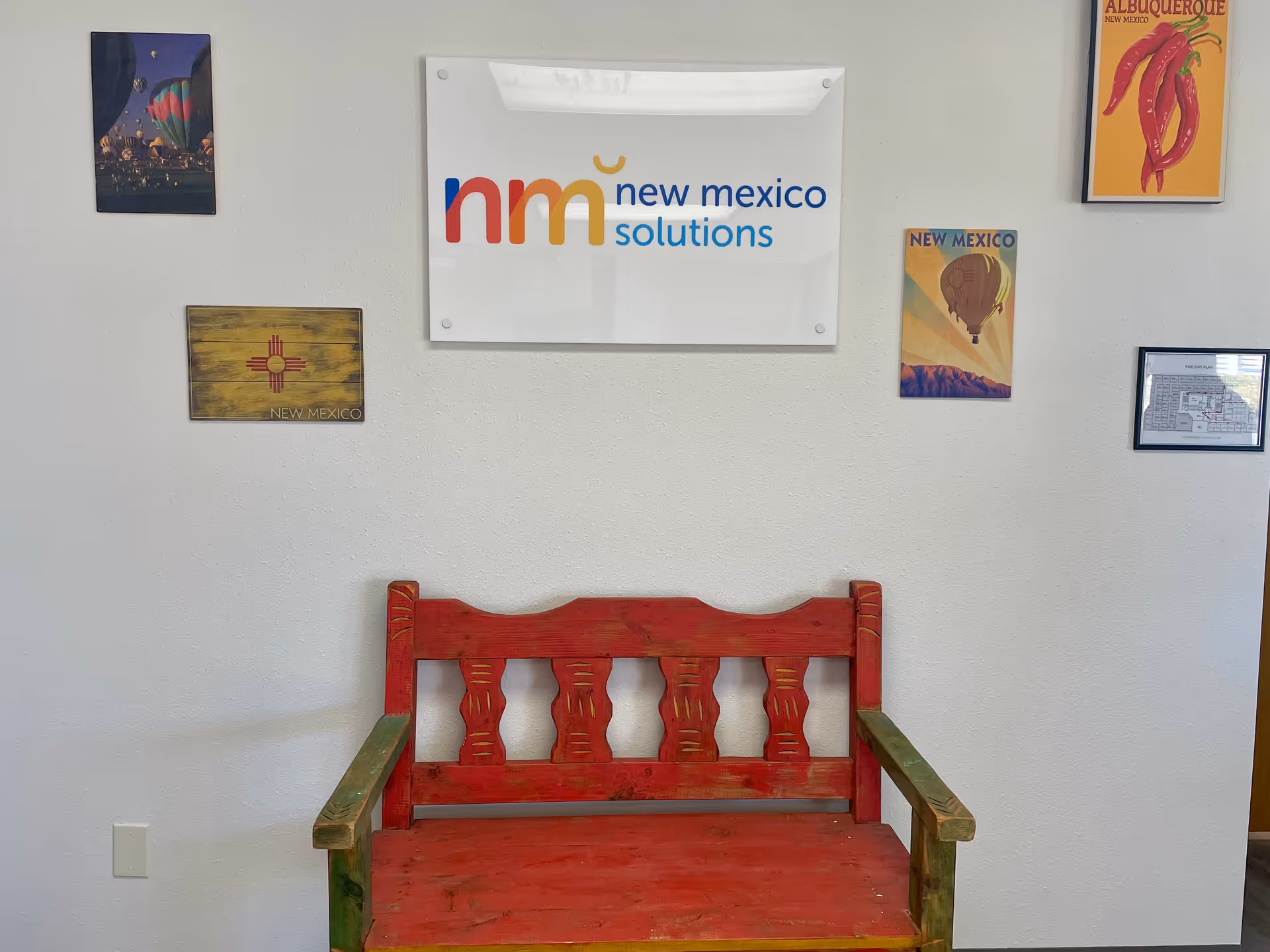 Interior wall with New Mexico Solutions sign and red wooden bench