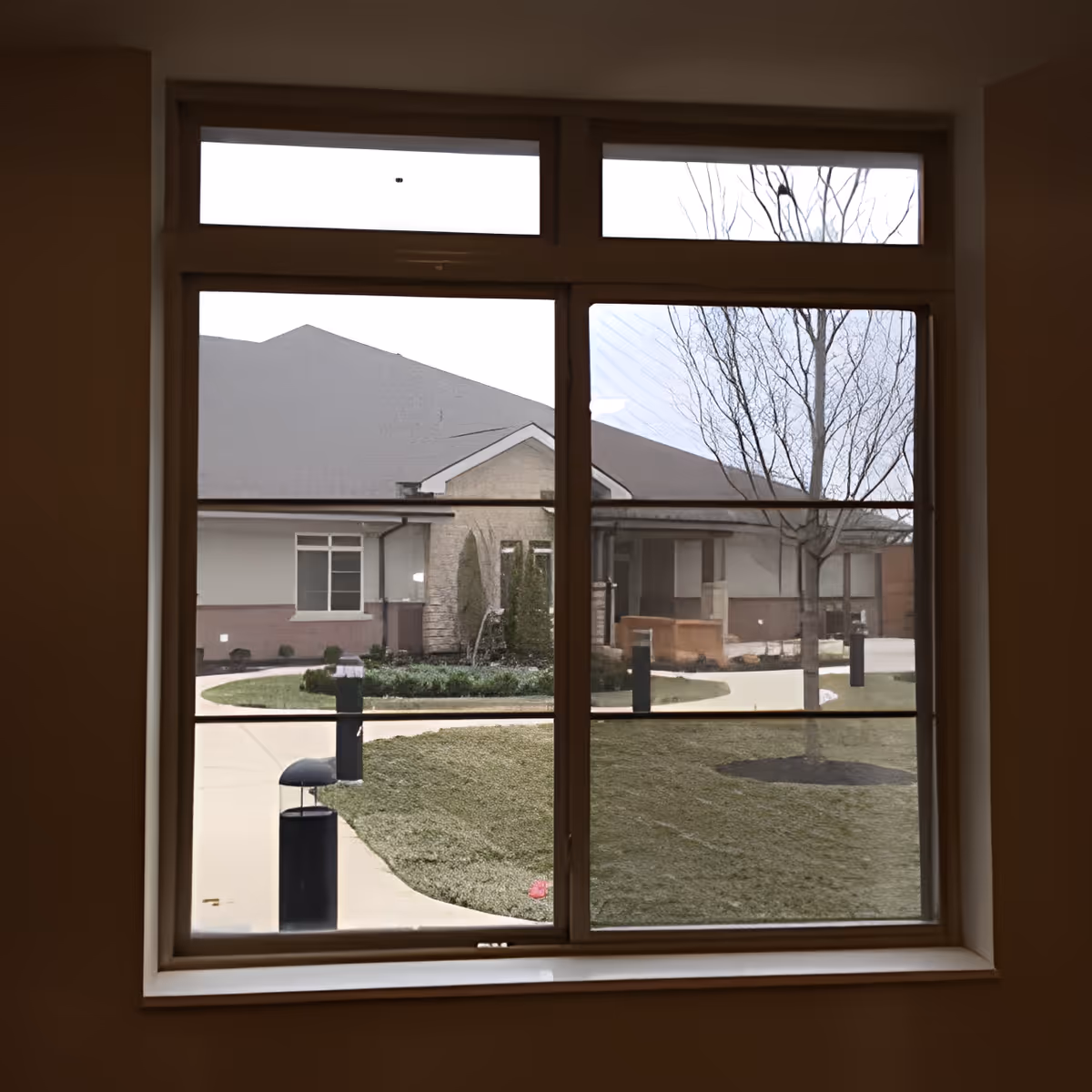 View through a large window onto a courtyard and the front of a single-story building with walkways and landscaping.