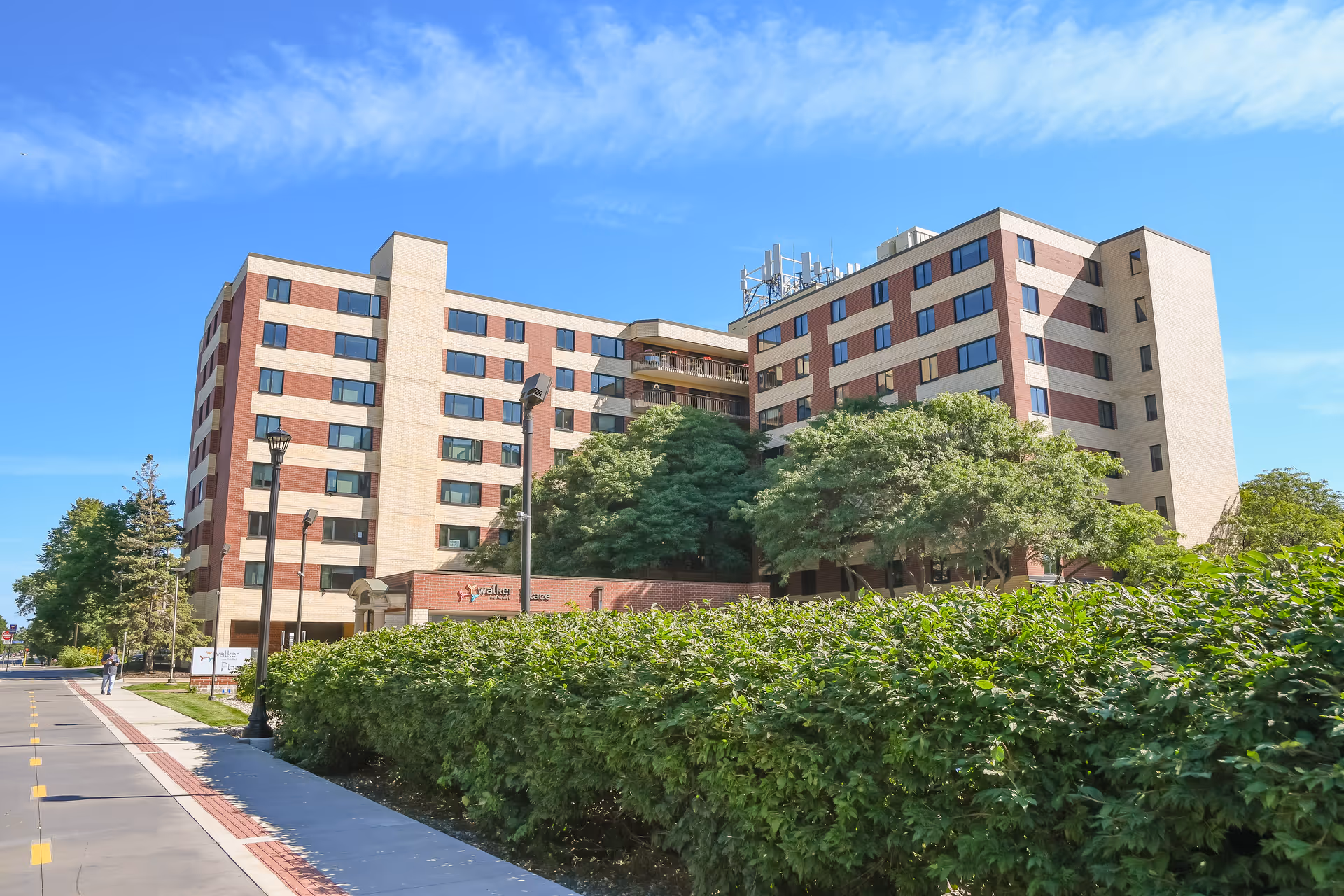 A multi-story brick senior living facility with manicured hedges under a blue sky.