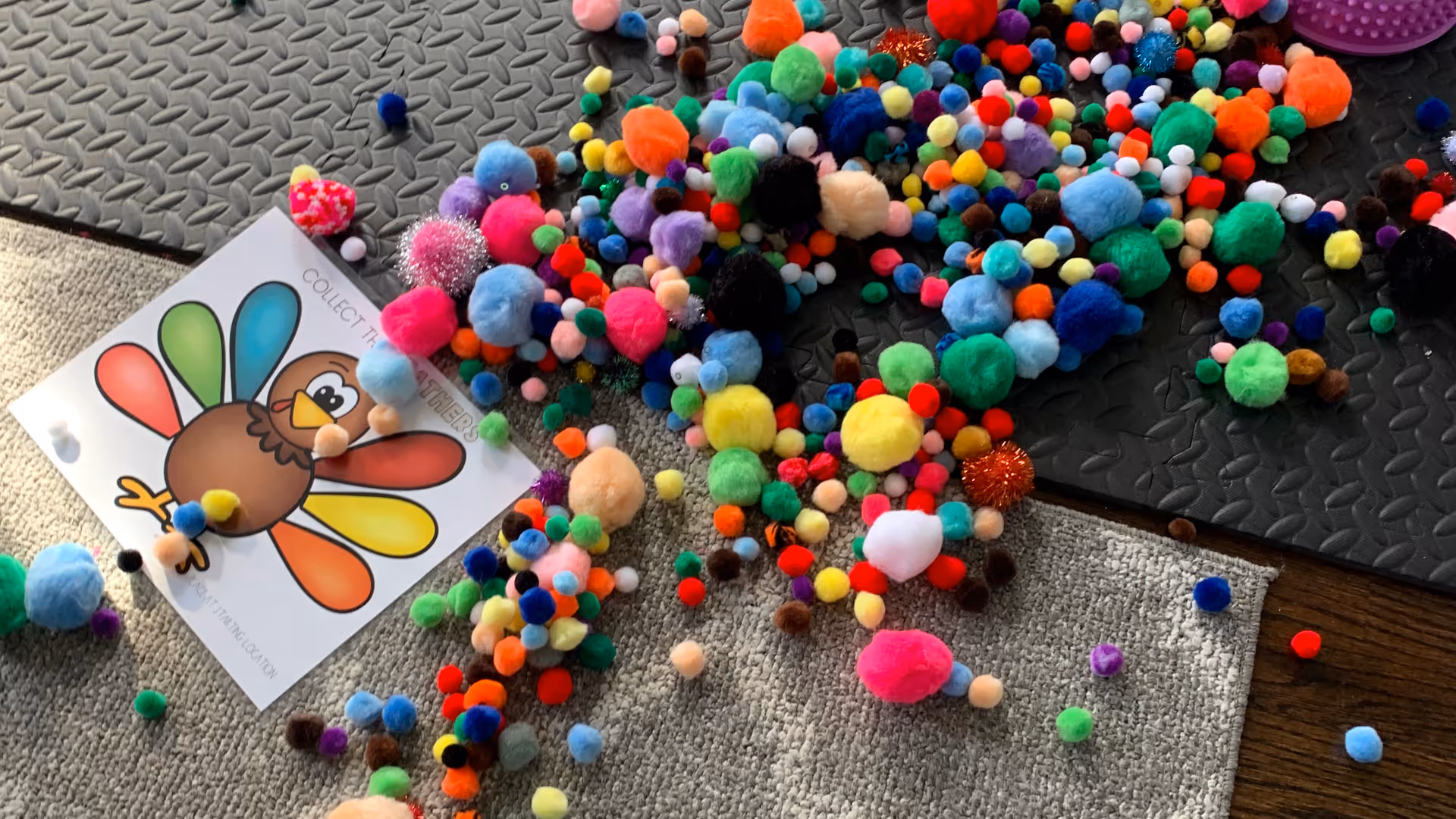 Colorful pom-poms and a turkey craft spread on a textured indoor floor mat.